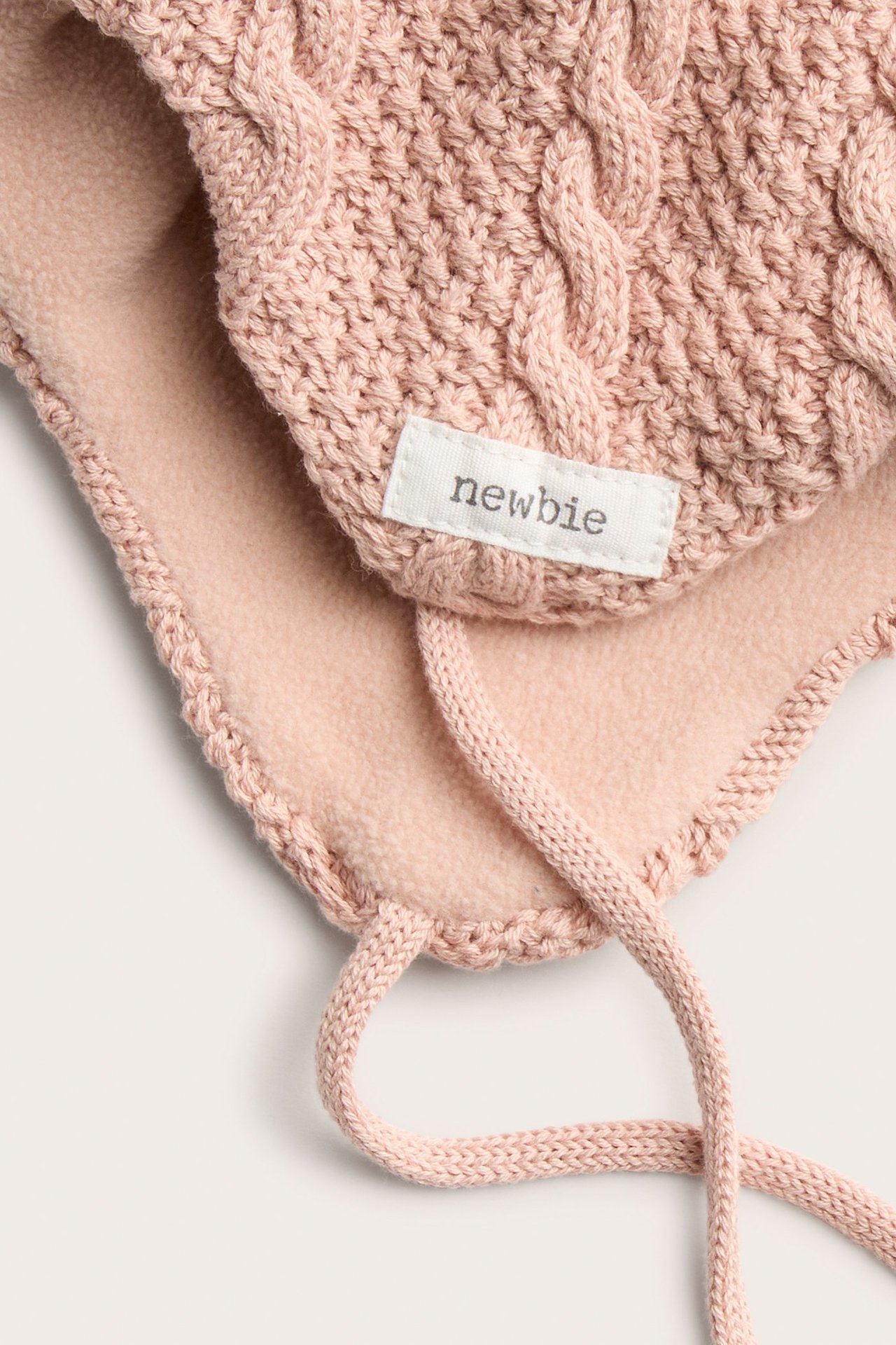 Nahaufnahme einer rosa Zopfstrick-Babymütze mit Fleece-Futter und Bindebändern.