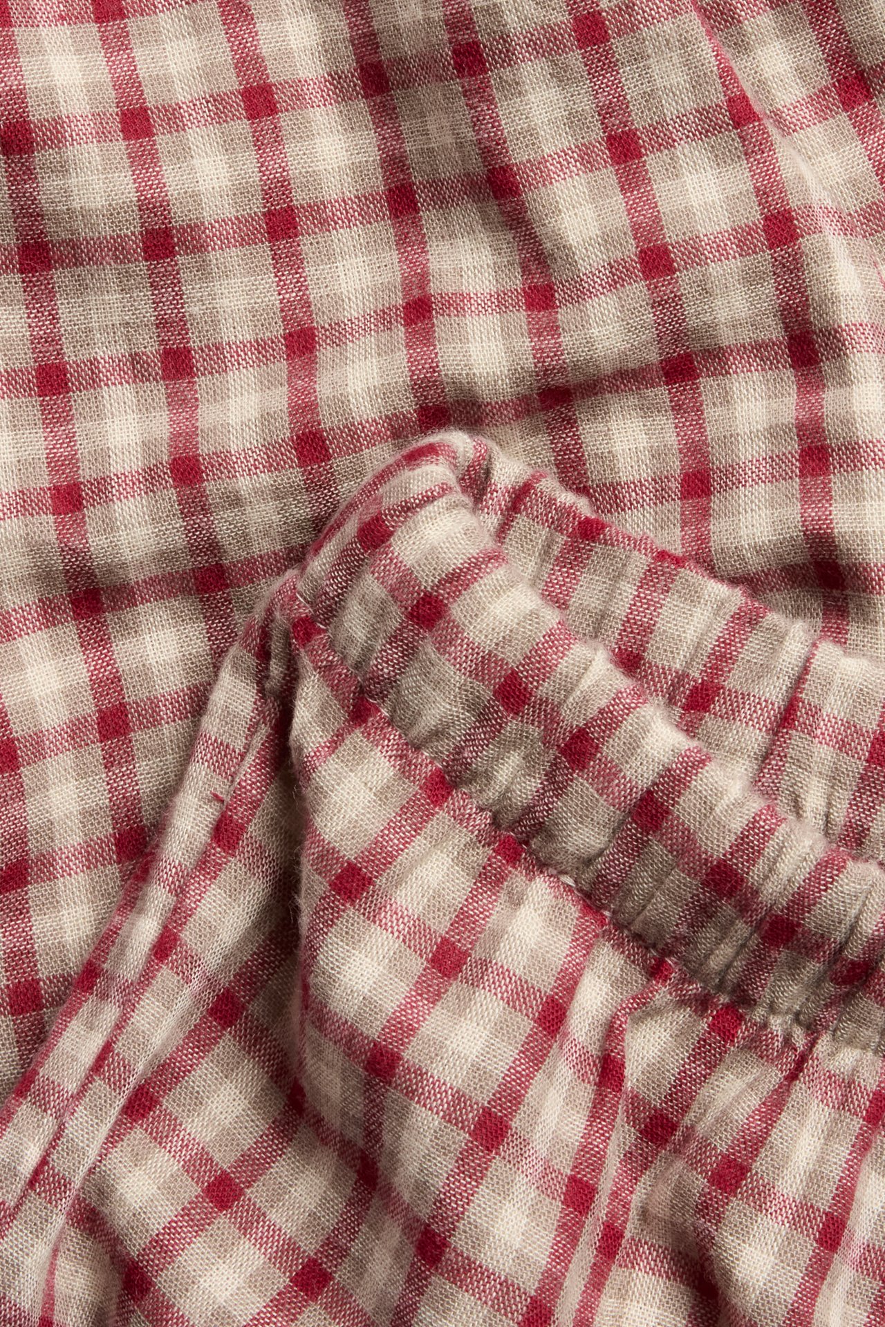 Nahaufnahme von rot-beigen karierten Baumwoll-Leggings mit elastischem, gerafftem Detail.