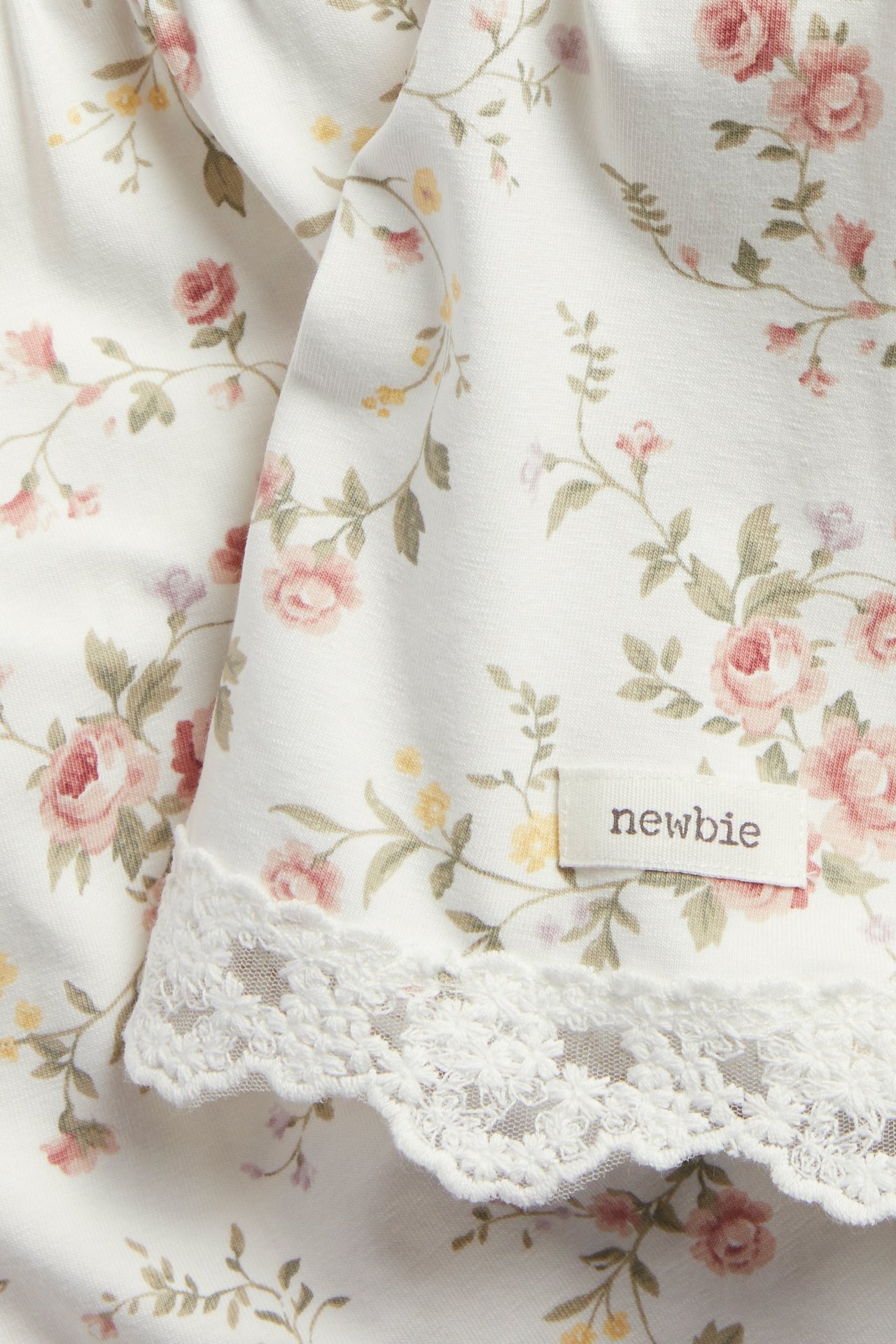 Nahaufnahme eines cremefarbenen, geblümten Strickkleides mit rosa Rosen und Spitzenbesatz.