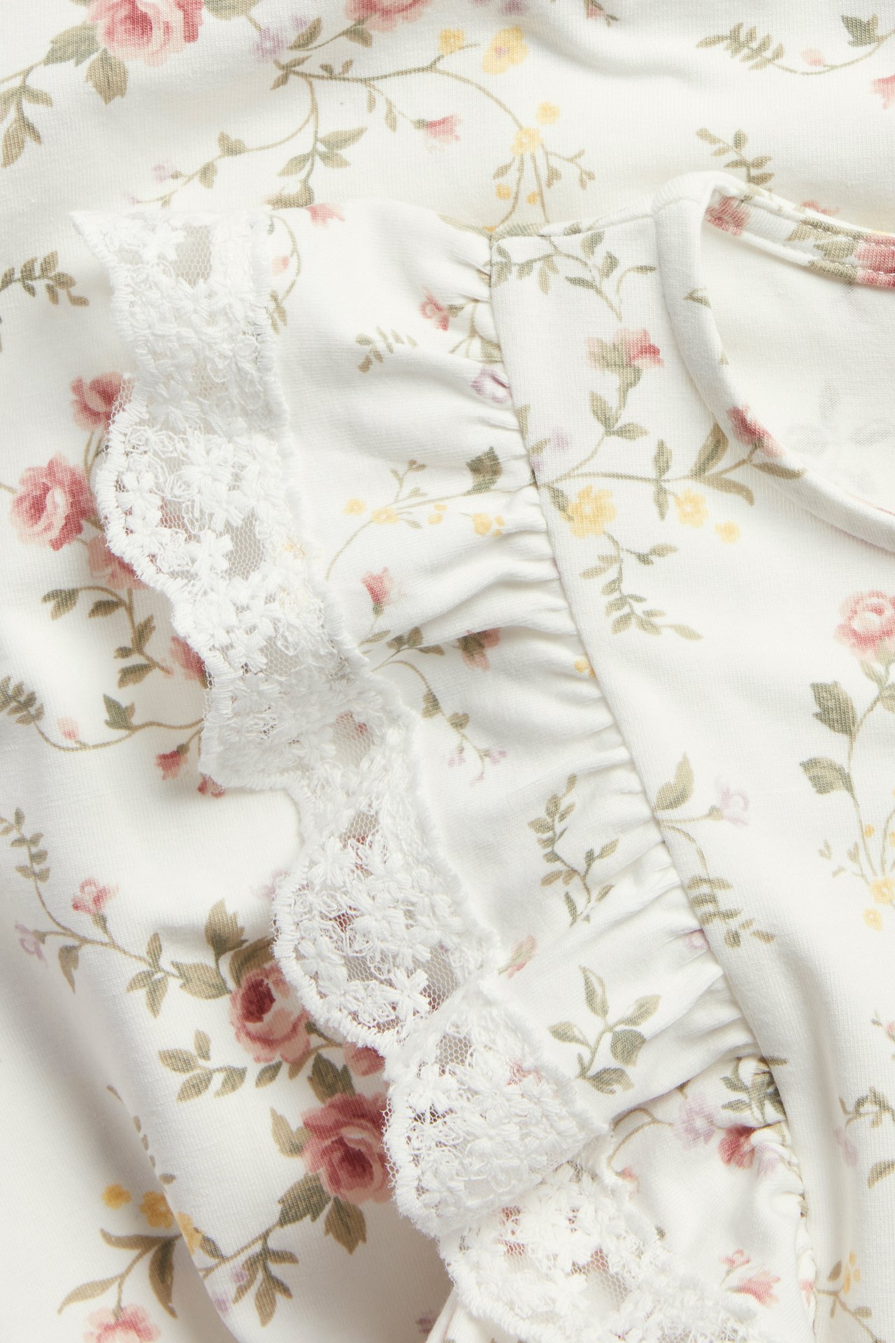 Close-up of an offwhite sleeveless floral jersey dress with lace and ruffle trim.