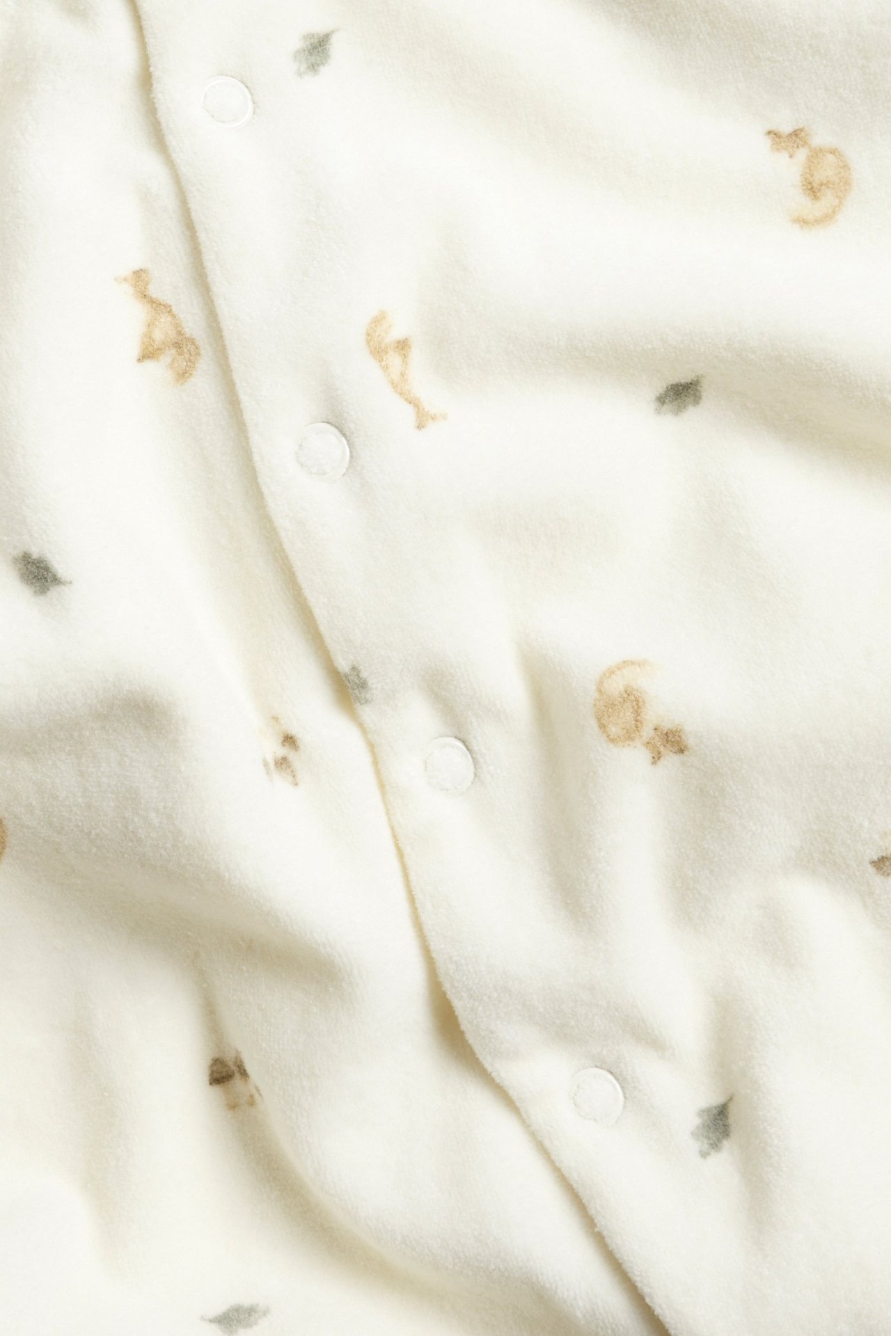 Nahaufnahme eines cremeweißen Baby-Velourpyjamas mit Fuchs- und Blattmuster und weißen Druckknöpfen.