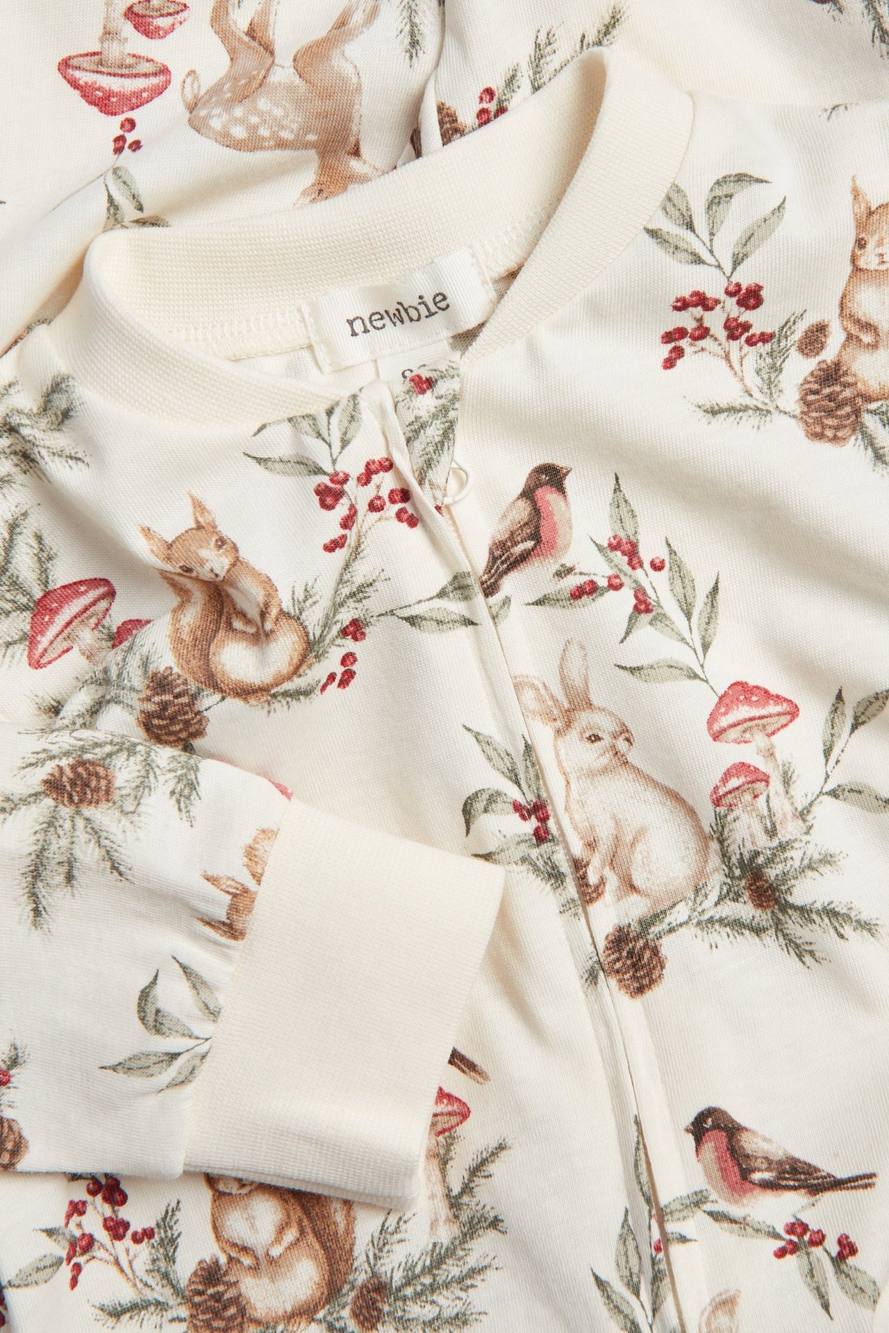 Close-up of a baby's off-white pyjamas with a festive animal pattern and a two-way zip.
