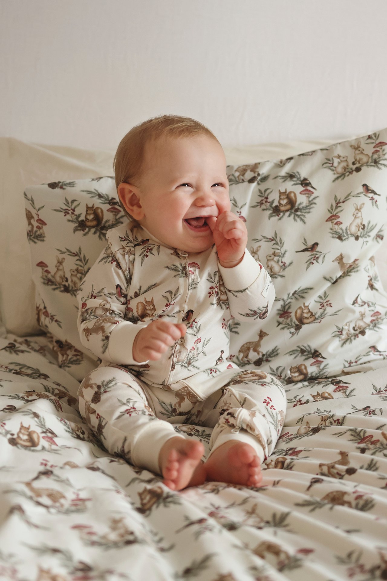 Front view of a laughing baby wearing an off-white cotton pyjamas with an animal print and front zipper.