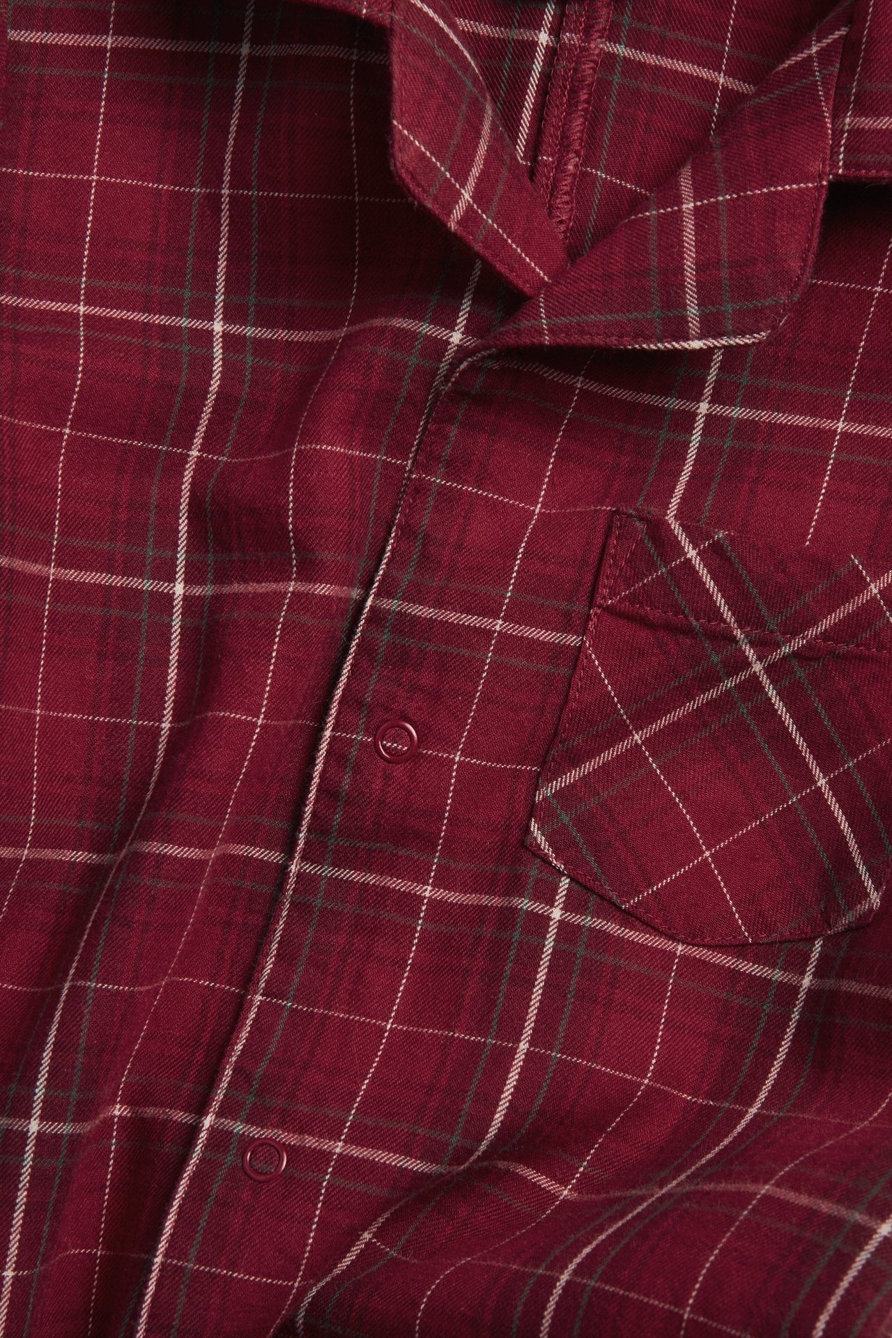 Nahaufnahme eines rot karierten Flanell-Pyjamaoberteils mit Druckknöpfen und Brusttasche.