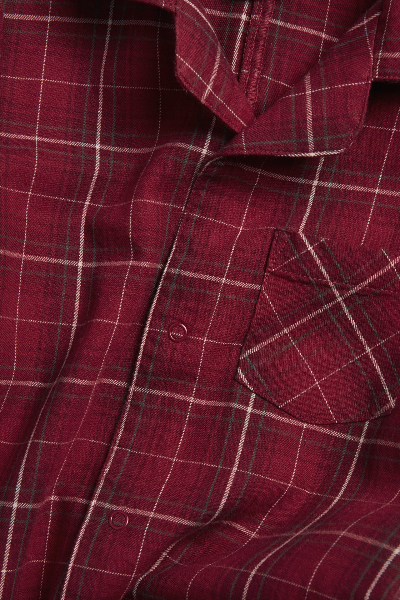 Close-up of a red checked flannel pajama top with snap buttons and a chest pocket.