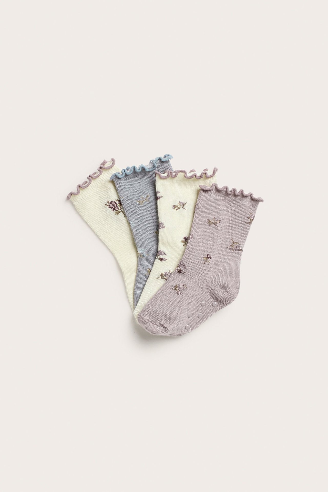 Vier geblümte Babysocken: helllila, hellblau und zwei cremefarbene, mit Rüschenbündchen und Antirutsch.