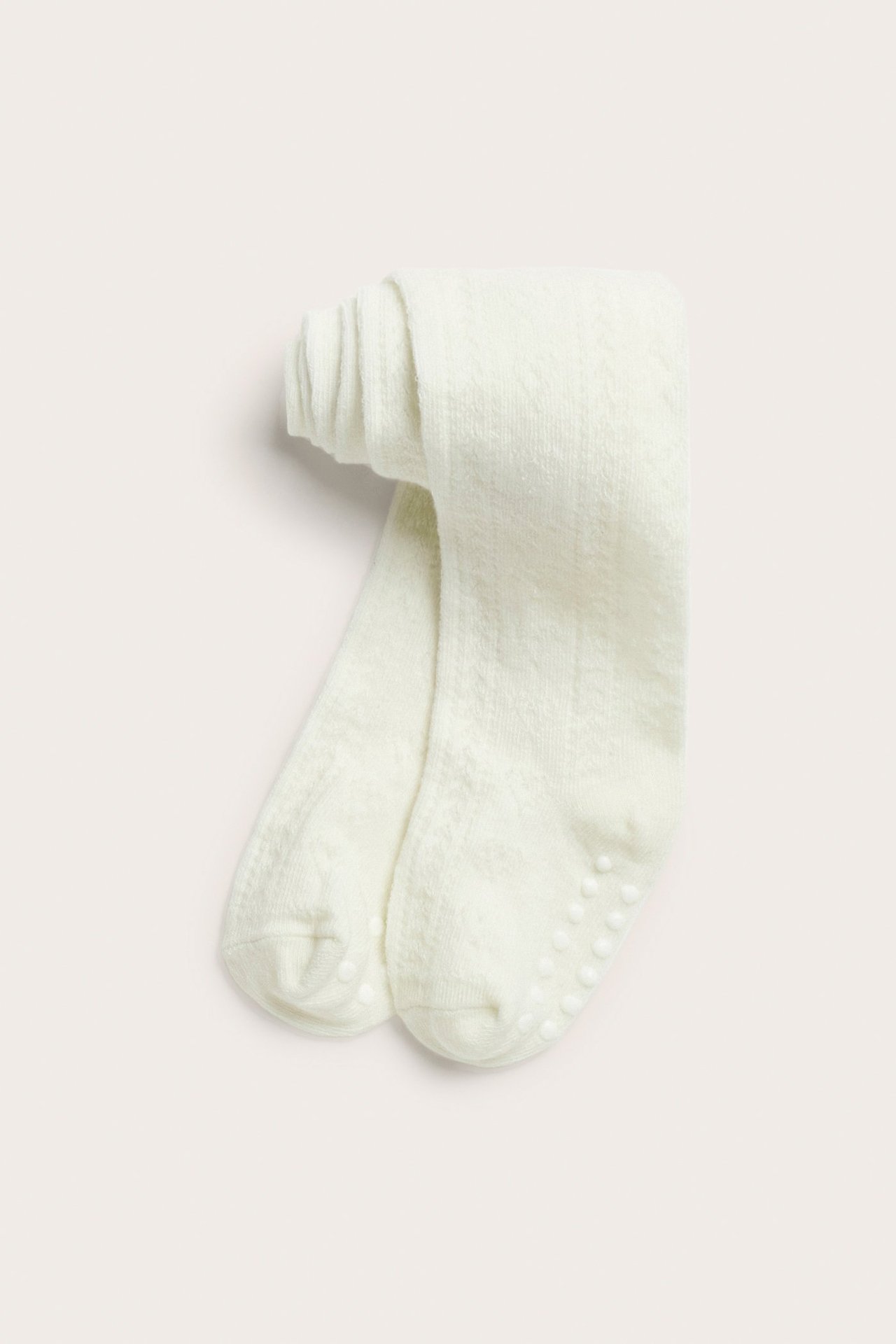 Vorderansicht gefalteter cremeweißer Babystrumpfhosen mit Lochmuster und Antirutsch-Noppen an den Sohlen.