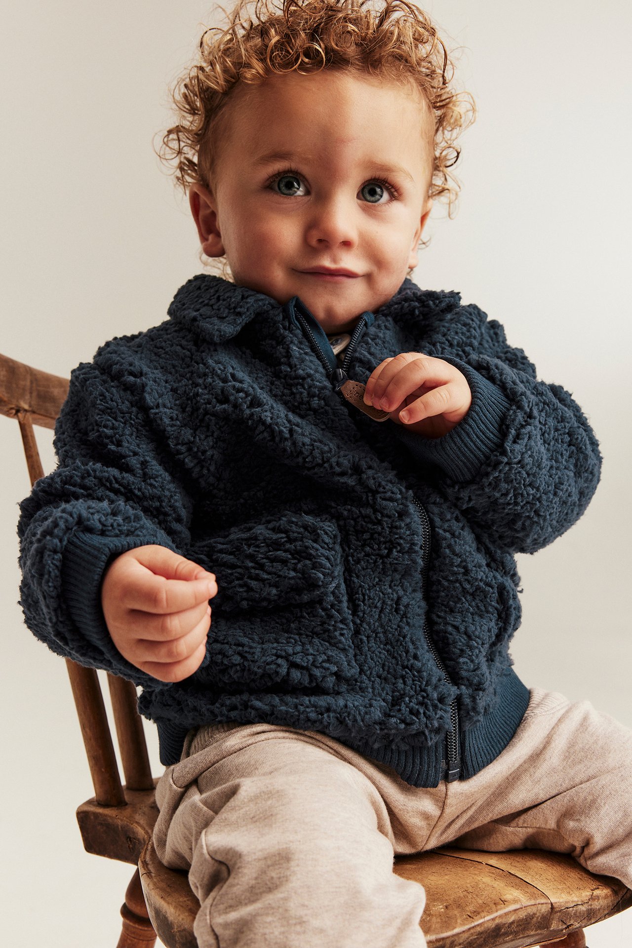 Front view: baby in dark blue pile jacket with collar, full zip, pockets, and light beige pants.