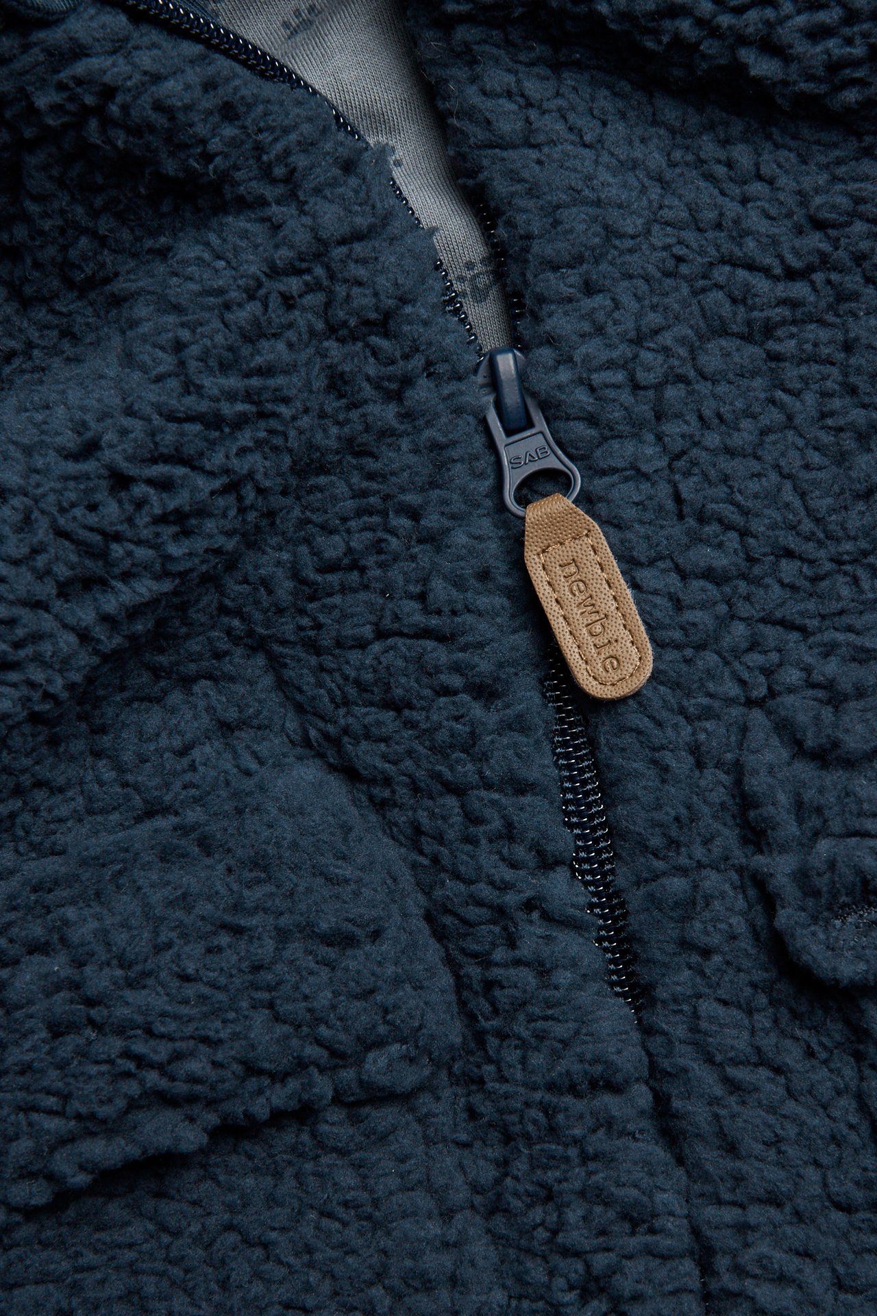 Close-up of a dark blue pile jacket, featuring a front zipper with a brown branded pull tab.