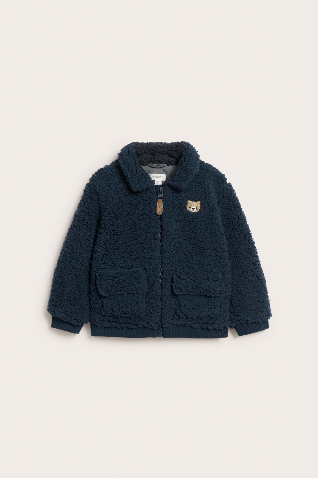 Front view of a dark blue kid's pile jacket with a zipper, two patch pockets, and a small bear embroidery.