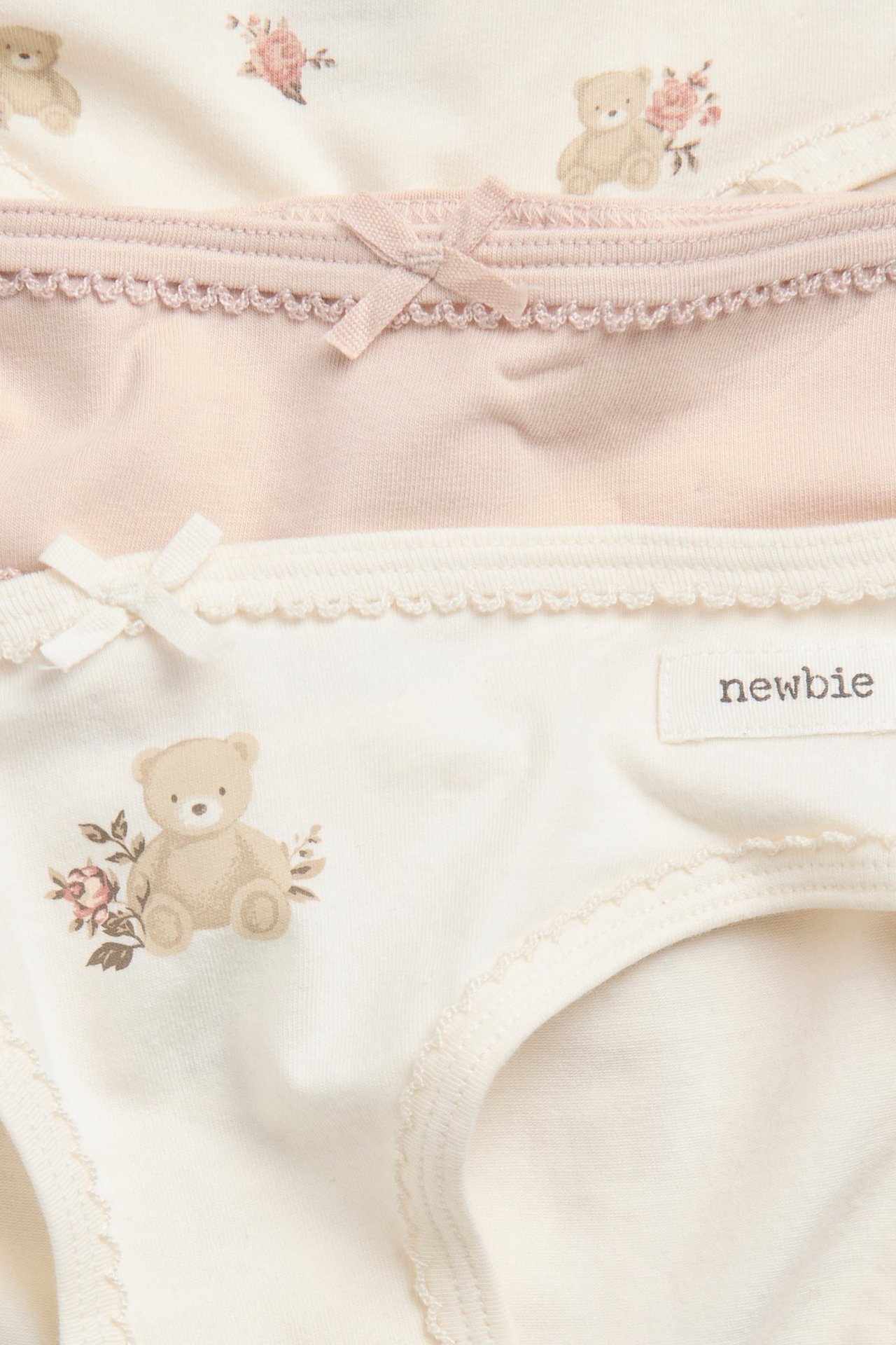 Nahaufnahme von drei Kinder-Jersey-Slips: einer rosa, zwei cremefarben mit Bären- und Blumenmuster.