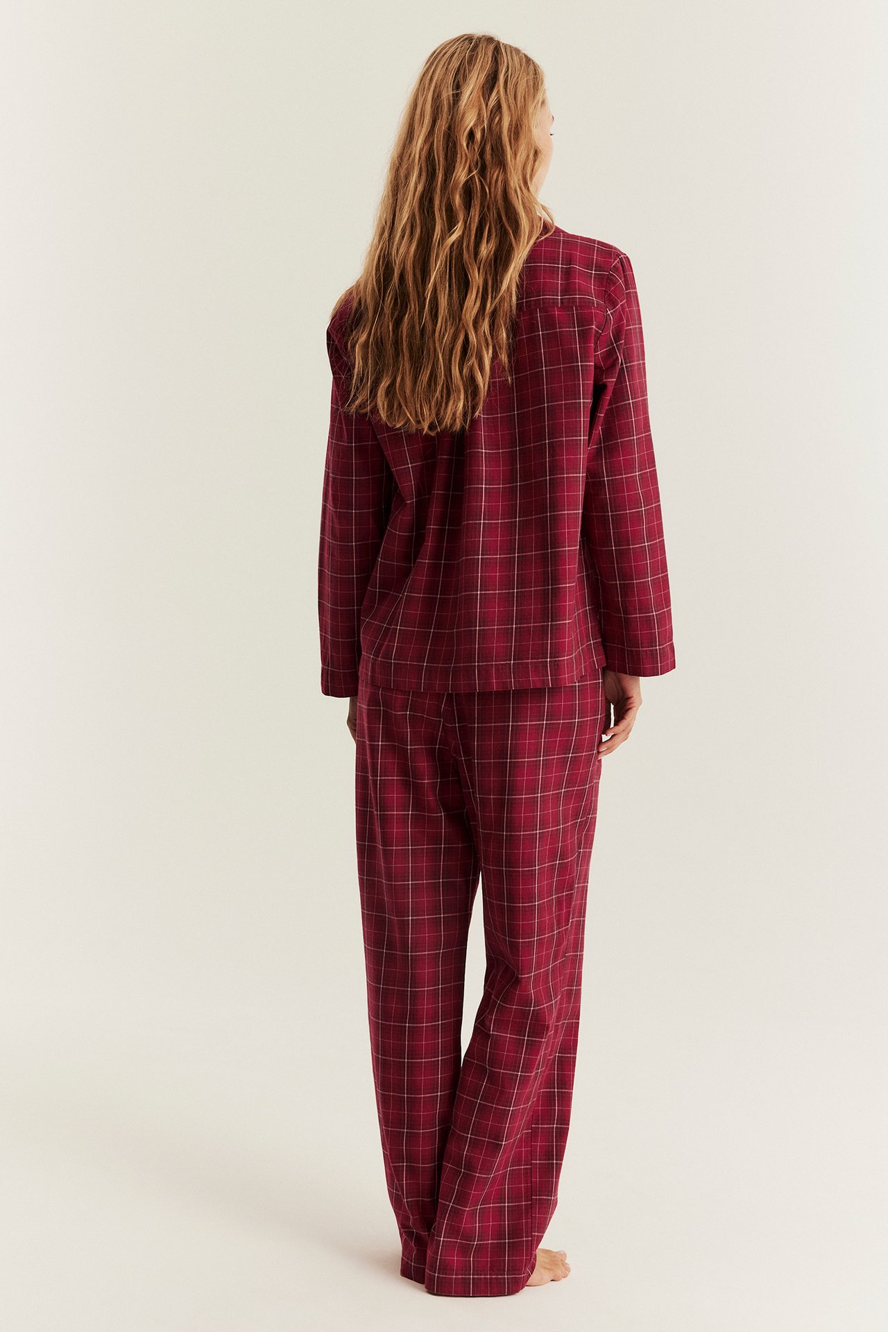 Rückenansicht einer Frau in einem rot karierten Flanell-Pyjama-Set mit Hemd und passender Hose.