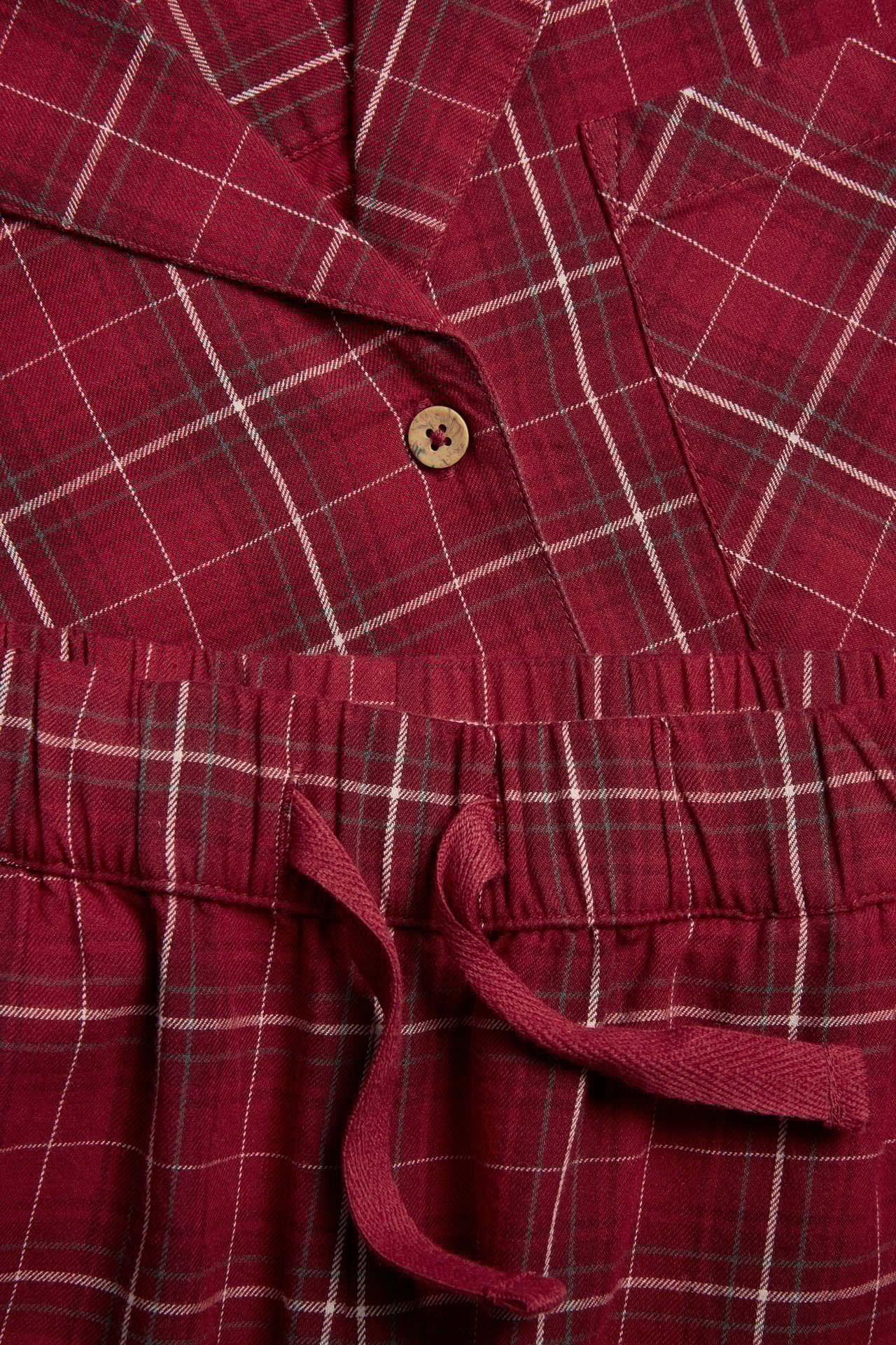 Nahaufnahme eines roten karierten Flanell-Pyjamas für Damen mit Knopf-Oberteil und Tunnelzug-Hose.