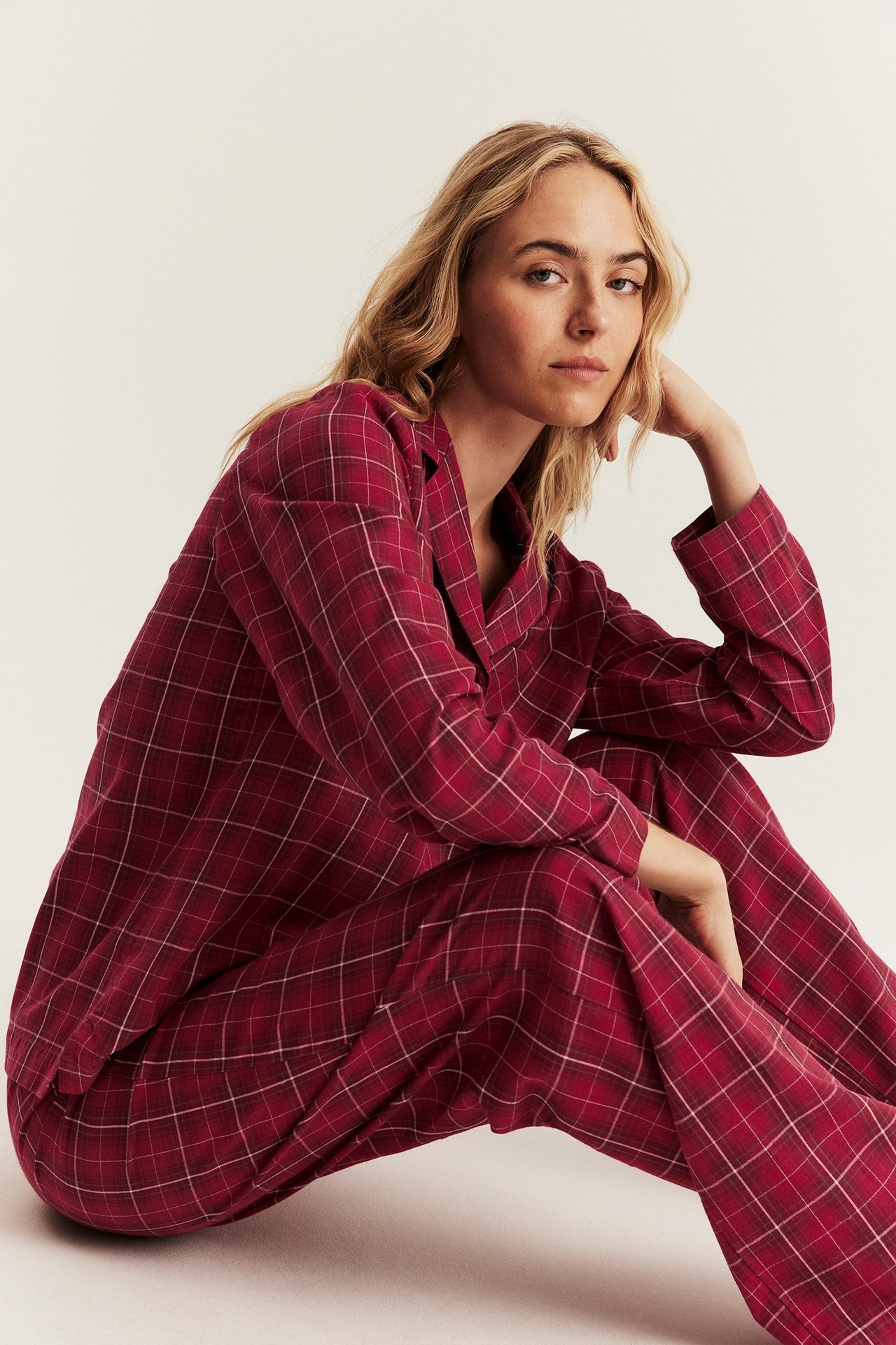 Sitzende Frau im roten karierten Flanell-Pyjama-Set mit klassischem Oberteil, Frontansicht.