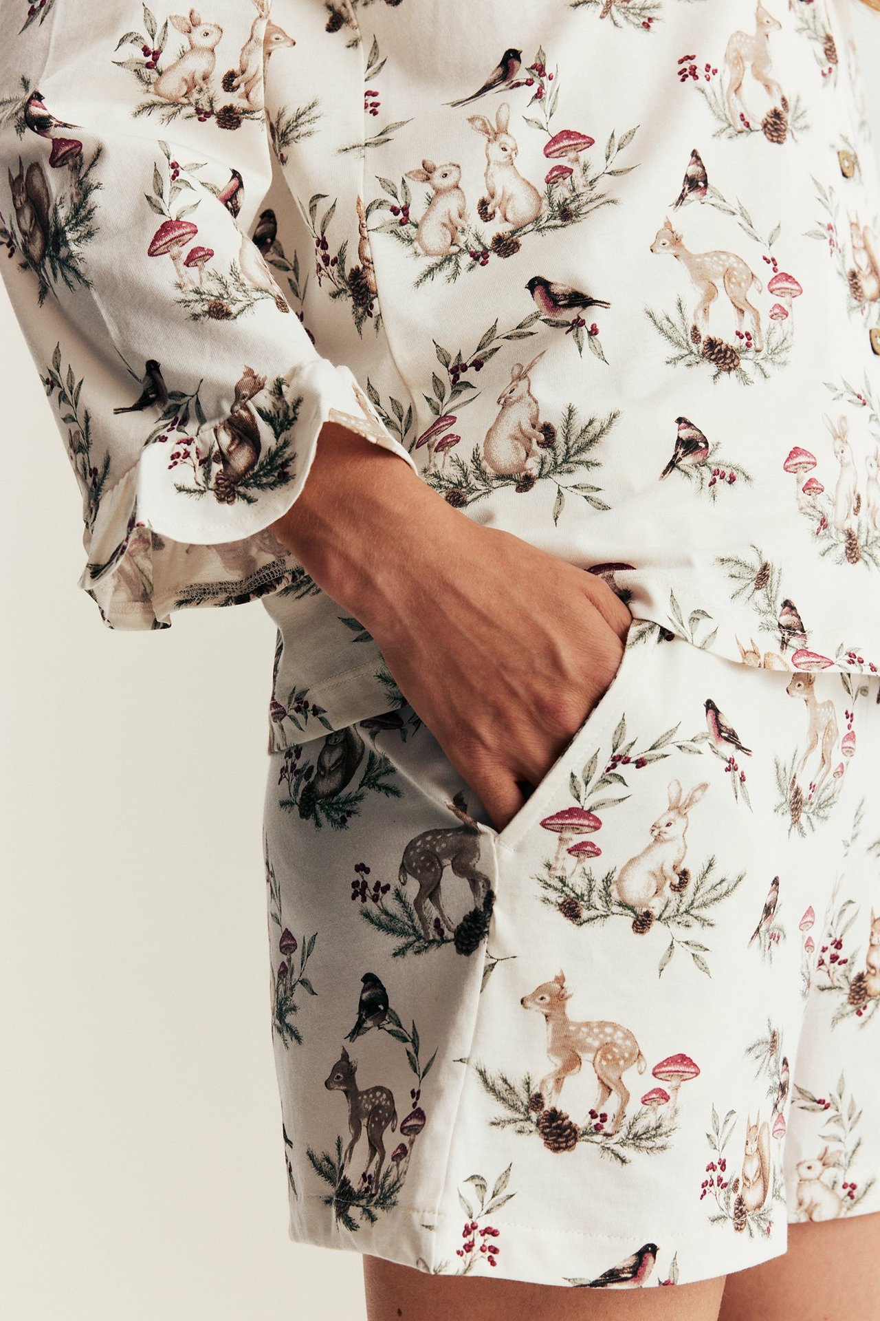 Close-up of a woman wearing off-white cotton pajamas with a forest animal print, ruffled cuffs and pockets.