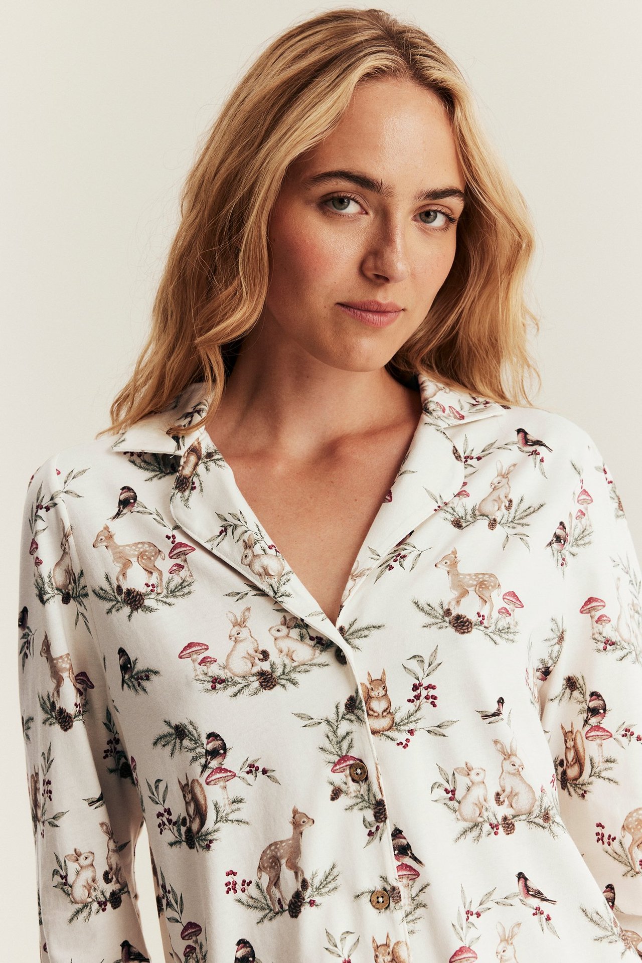 Close-up front view: Woman in off-white cotton pajama top, festive forest animal print, button-front.