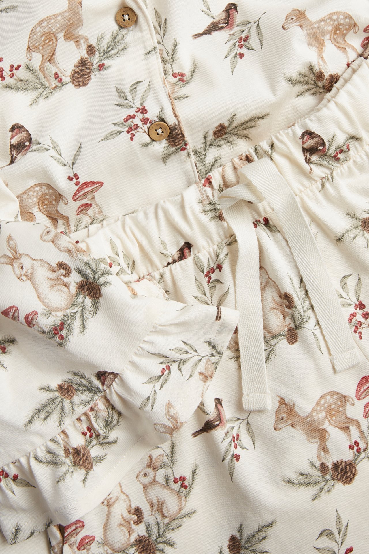 Nahaufnahme eines naturweißen Baumwollpyjamas mit Knöpfen, Kordelzug und festlichem Tiermuster.