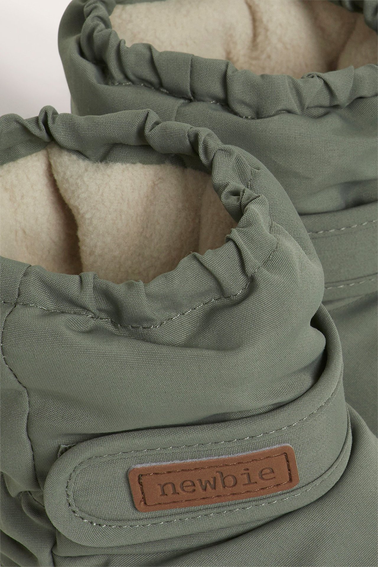 Close-up of dark green padded baby booties with a soft fleece lining and adjustable strap.