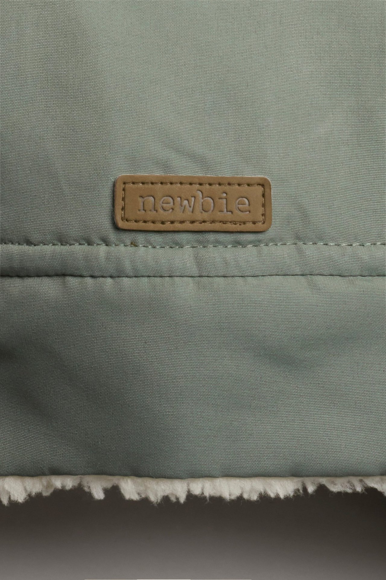 Nahaufnahme einer dunkelgrünen Baby-/Kinder-Wintermütze mit braunem Etikett und weißem Teddyfutter.