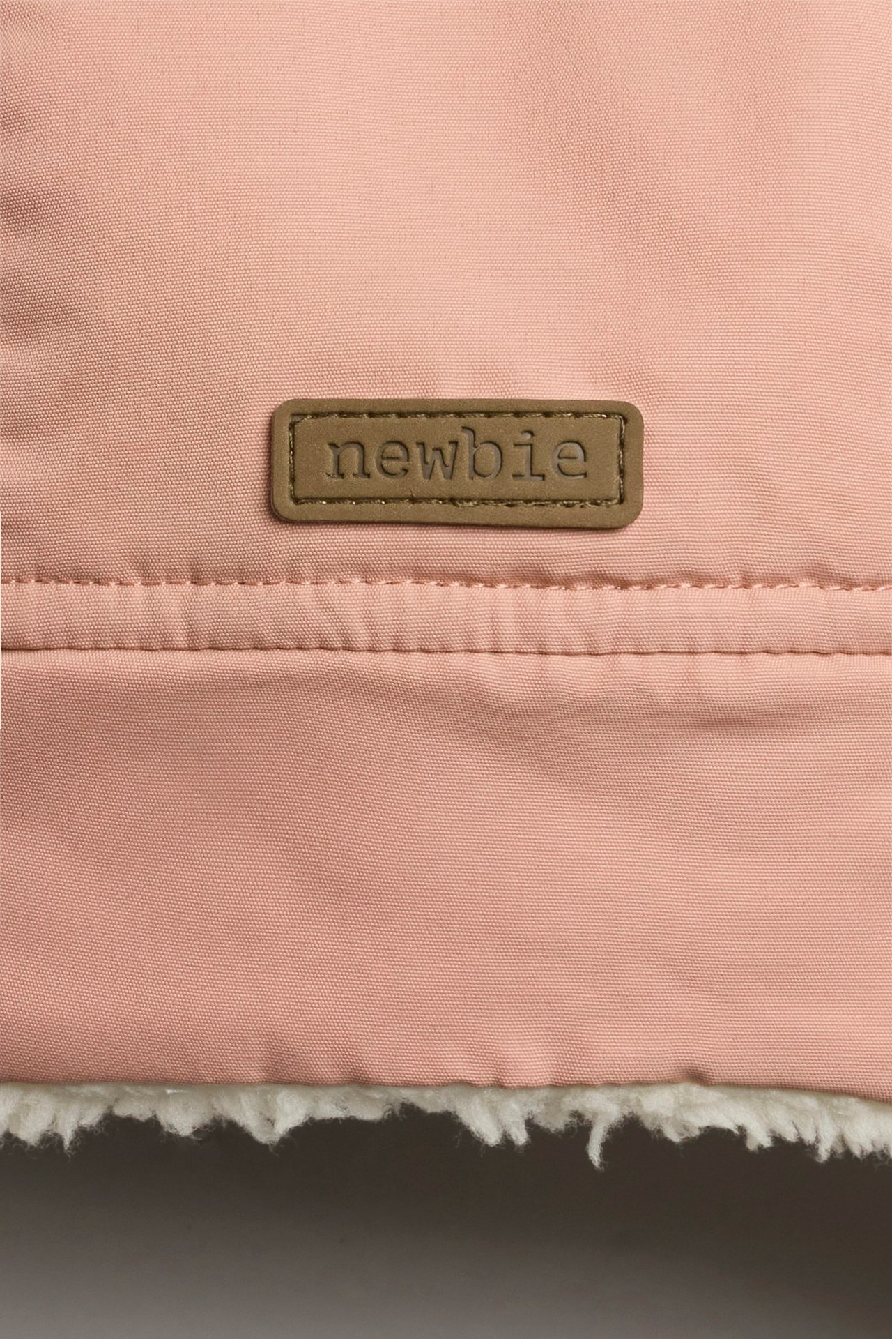 Nahaufnahme des rosa Wintermützenstoffs mit Newbie-Etikett und weißem Teddyfutter.