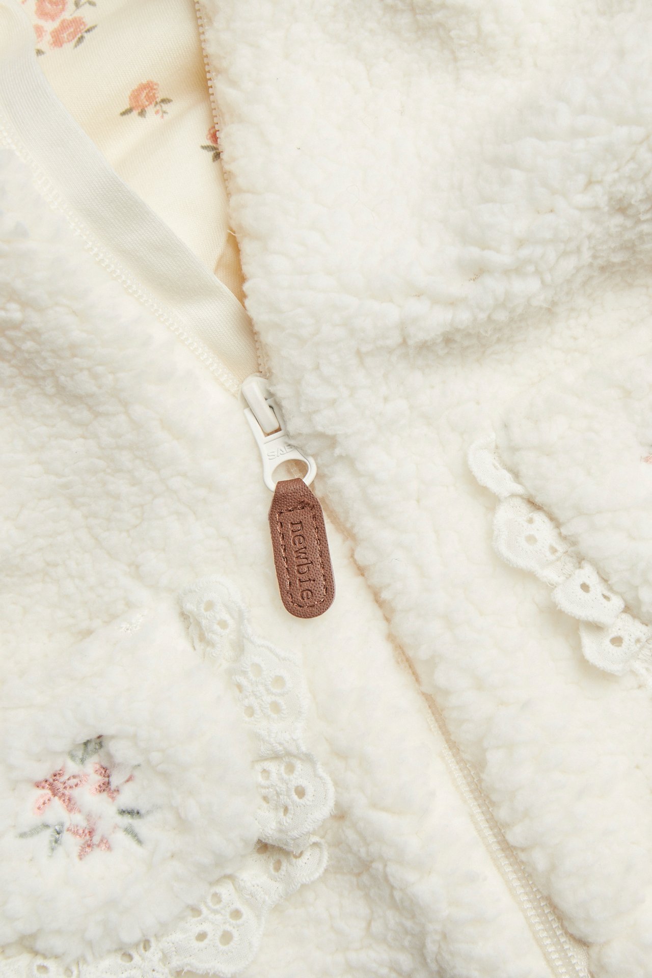 Close-up front view: off-white kid's pile jacket with a zipper, lace trim, floral embroidery, patterned lining.