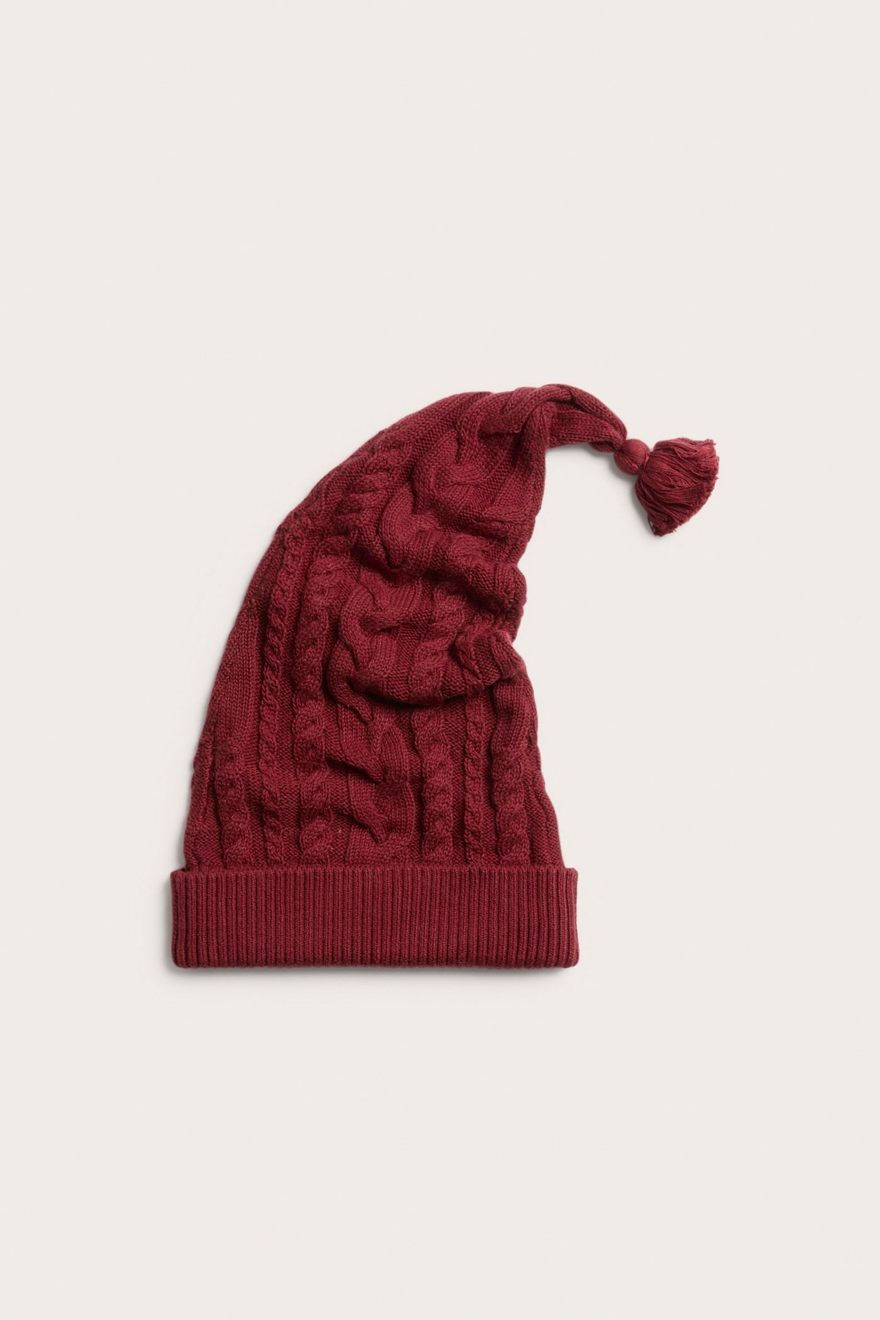 Front view of a red cable-knit cotton Santa hat with a ribbed brim and a tassel on top.