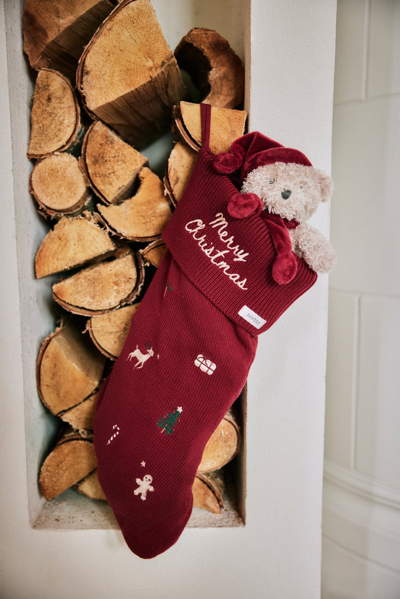 Close-up front view of a red knitted Christmas stocking with festive embroideries and a teddy bear inside.