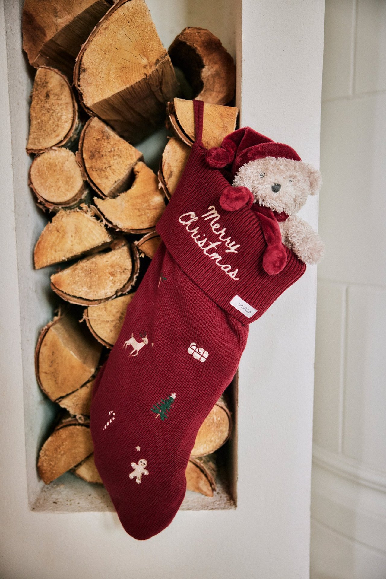 Close-up front view of a red knitted Christmas stocking with festive embroideries and a teddy bear inside.