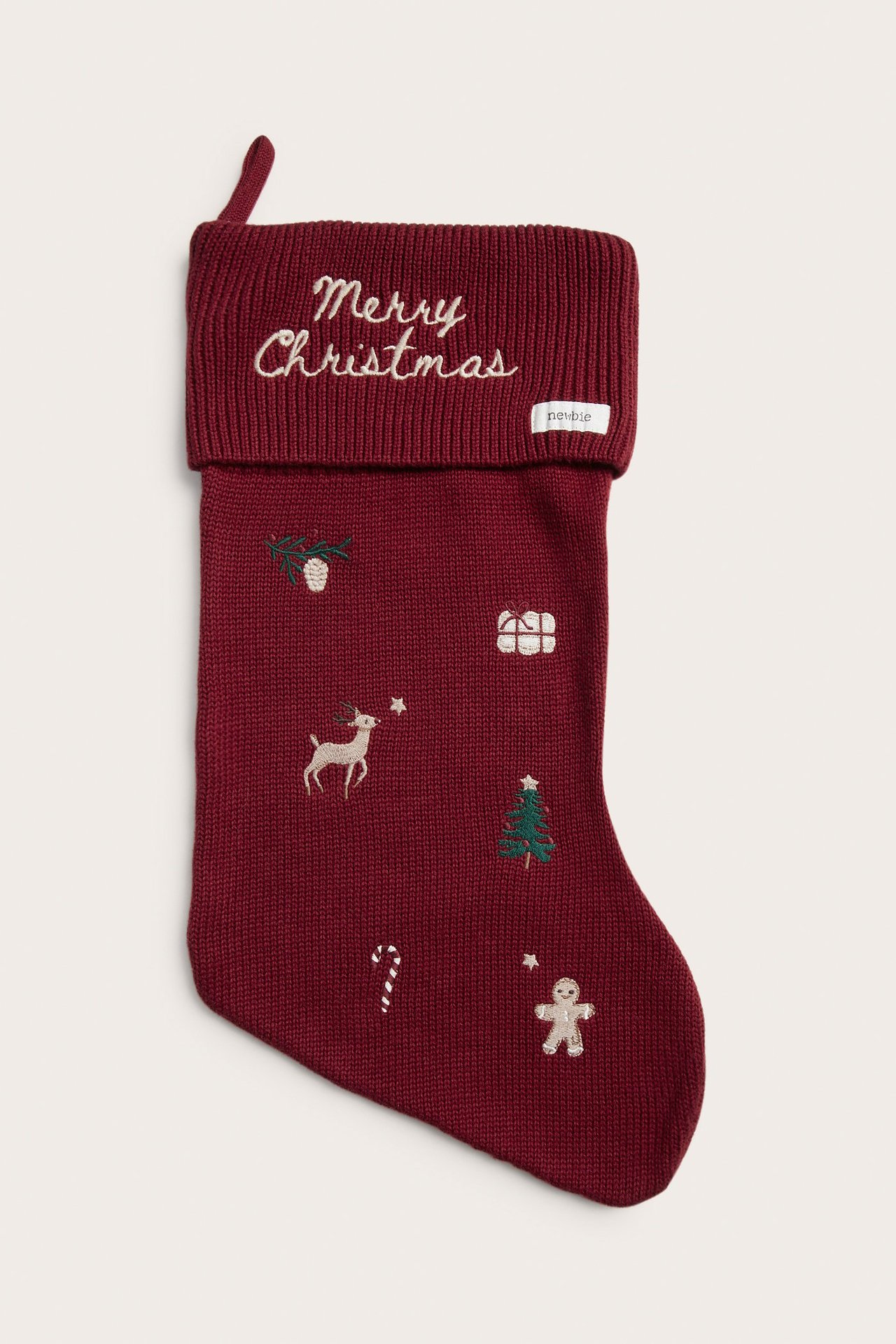 Front view of a red knitted cotton Christmas stocking with folded ribbed edge and festive embroideries.