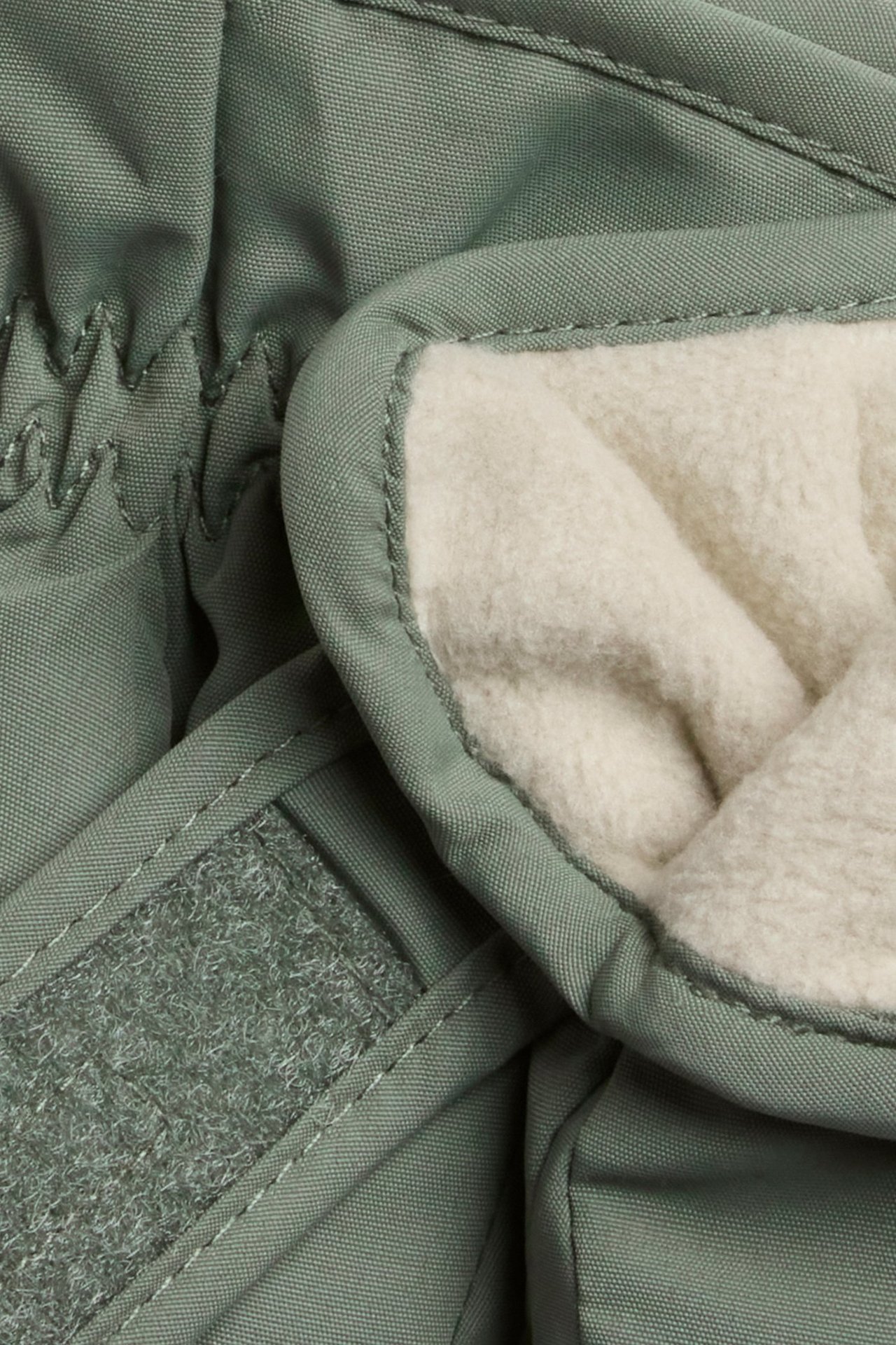 Nahaufnahme von dunkelgrünen wasserabweisenden Fäustlingen mit cremefarbenem Fleecefutter und Klettverschluss am Bündchen.