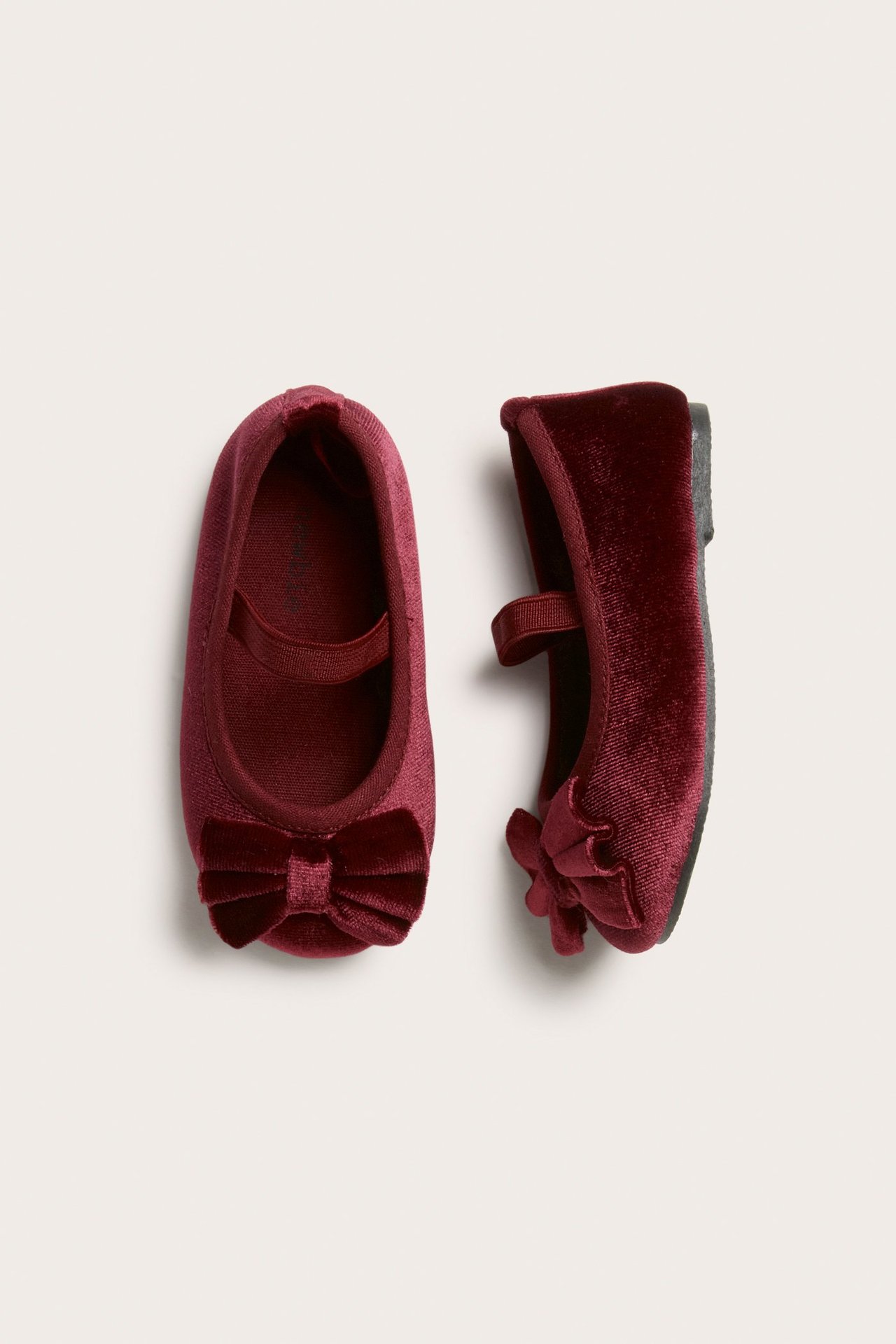Top view of a pair of red velvet kid's ballet flats with bows and elastic straps.