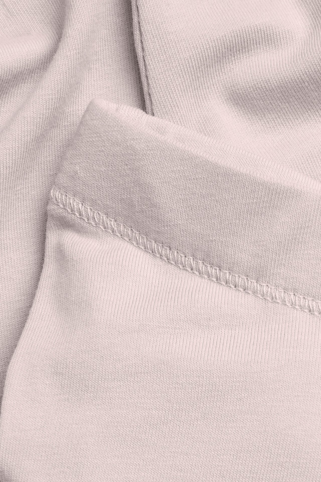 Nahaufnahme von hellbeigem geripptem Strickstoff mit sichtbaren Nähten.