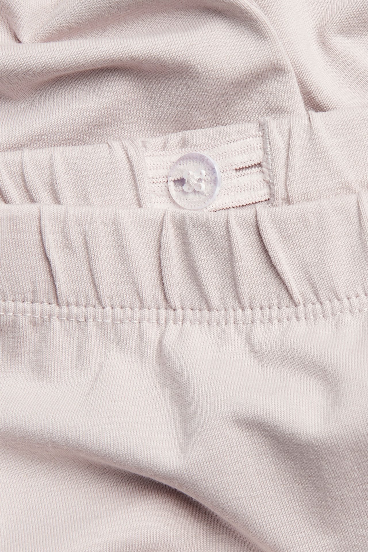 Close-up of light pink knit fabric with an adjustable elastic waistband and a clear button.