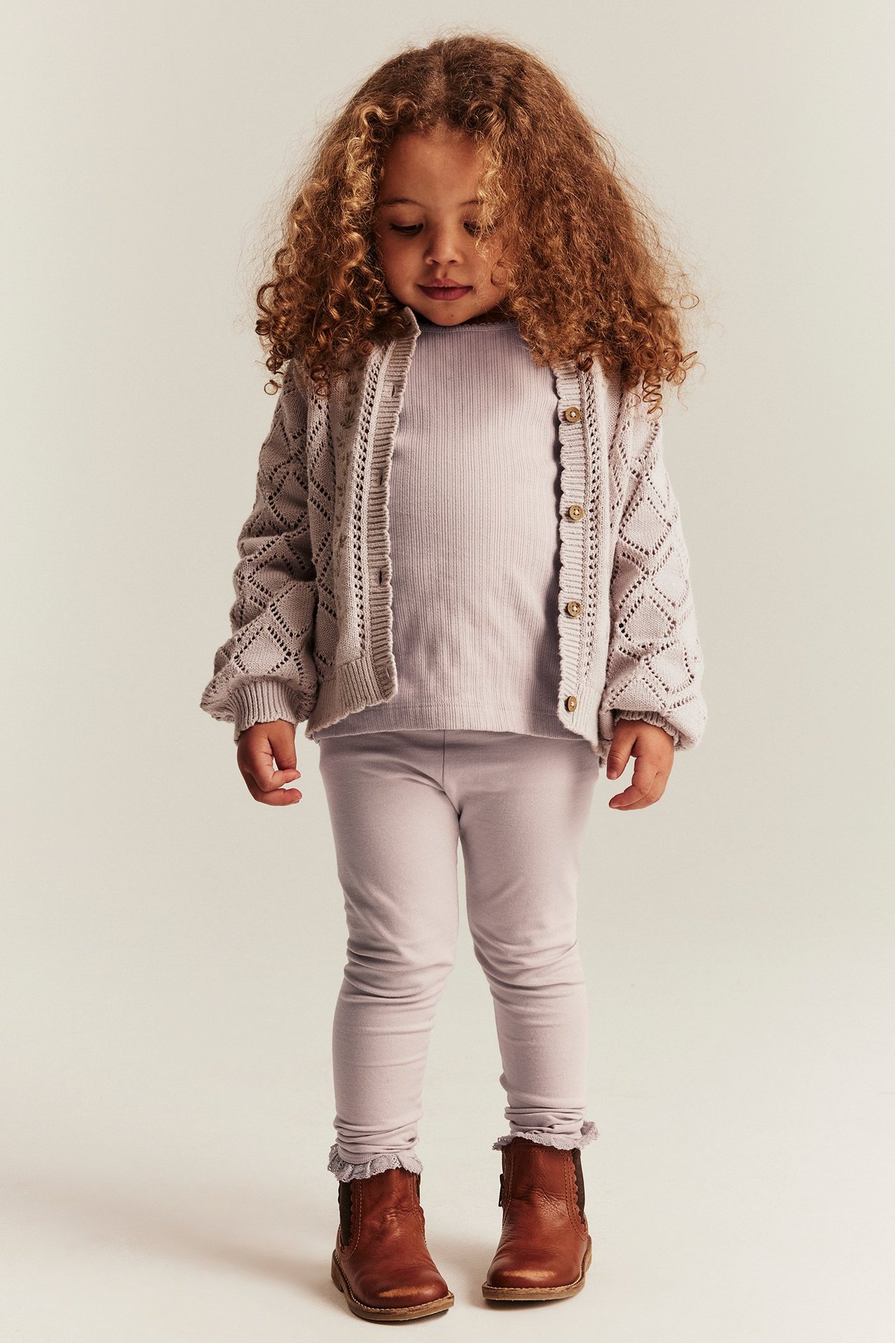 Vorderansicht: Kind in hellen lila Leggings mit Spitzenbesatz, geripptem Oberteil und offener Strickjacke.