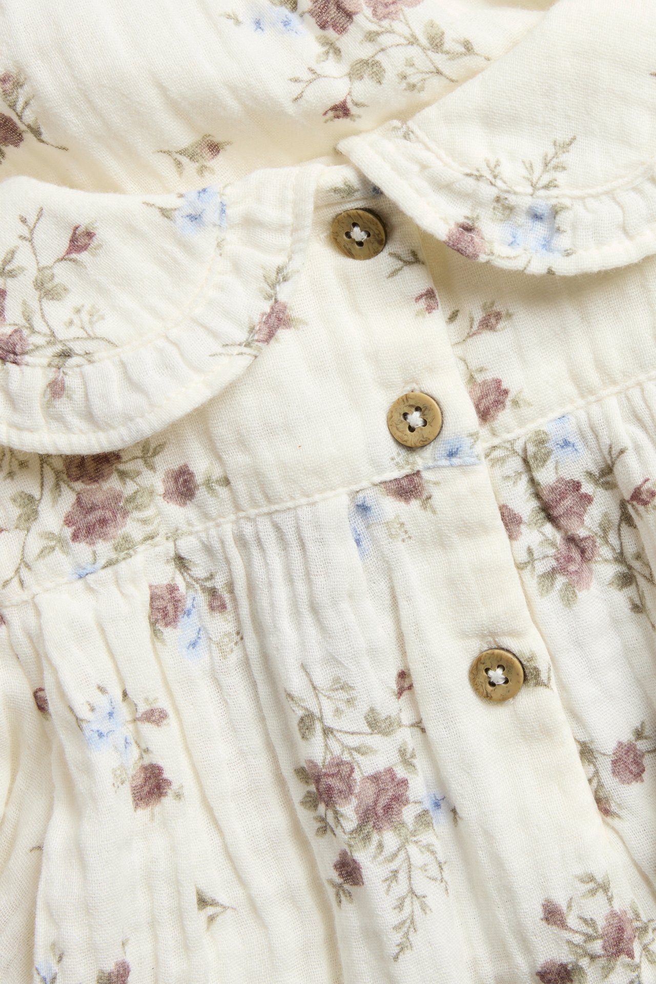 Close-up of baby's off-white floral blouse-body with ruffled collar and wooden buttons.