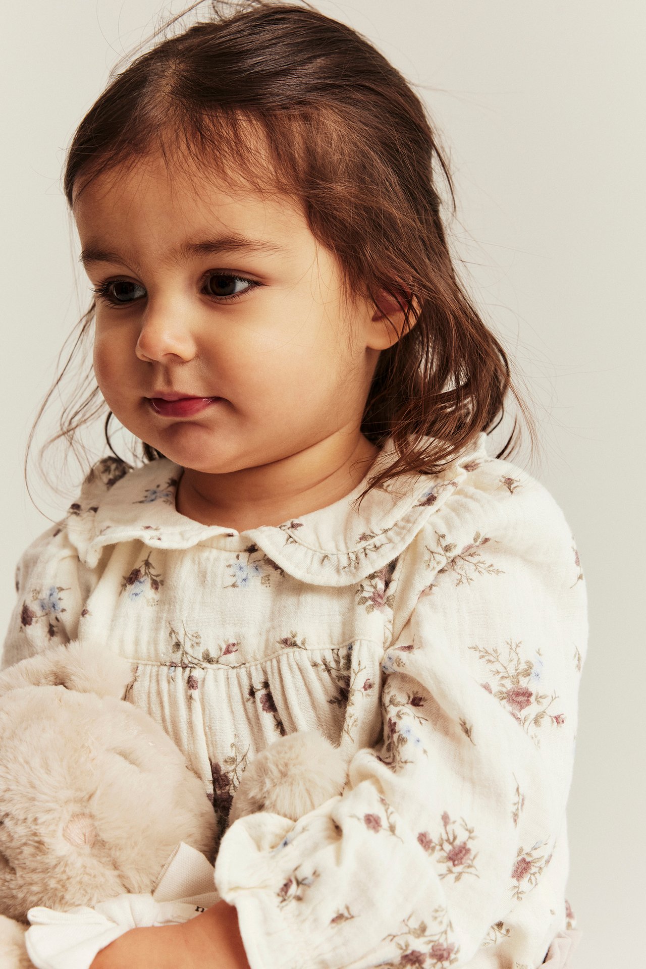 Close-up: baby wears an off-white floral blouse-bodysuit with ruffled collar and puff sleeves.
