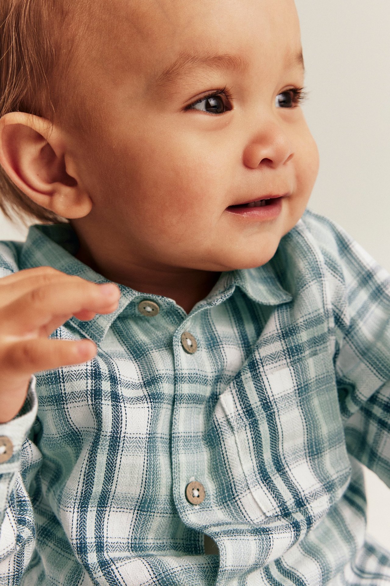 Nahaufnahme eines Babys in hellgrünem, kariertem Baumwoll-Shirt-Body mit Knöpfen.