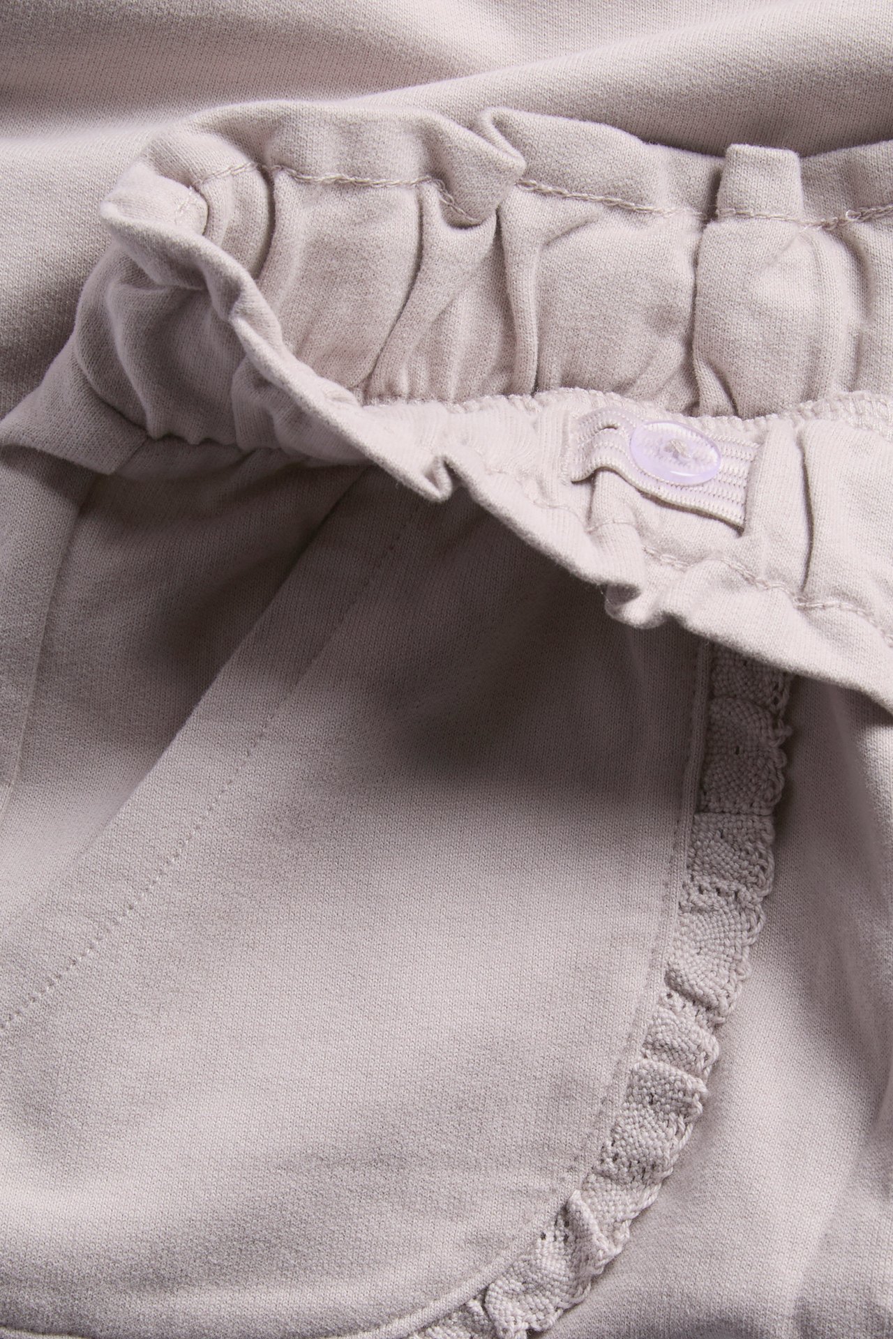 Nahaufnahme von beigefarbenen Kinder-Jersey-Shorts mit Rüschenbund und verstellbarem Knopf.