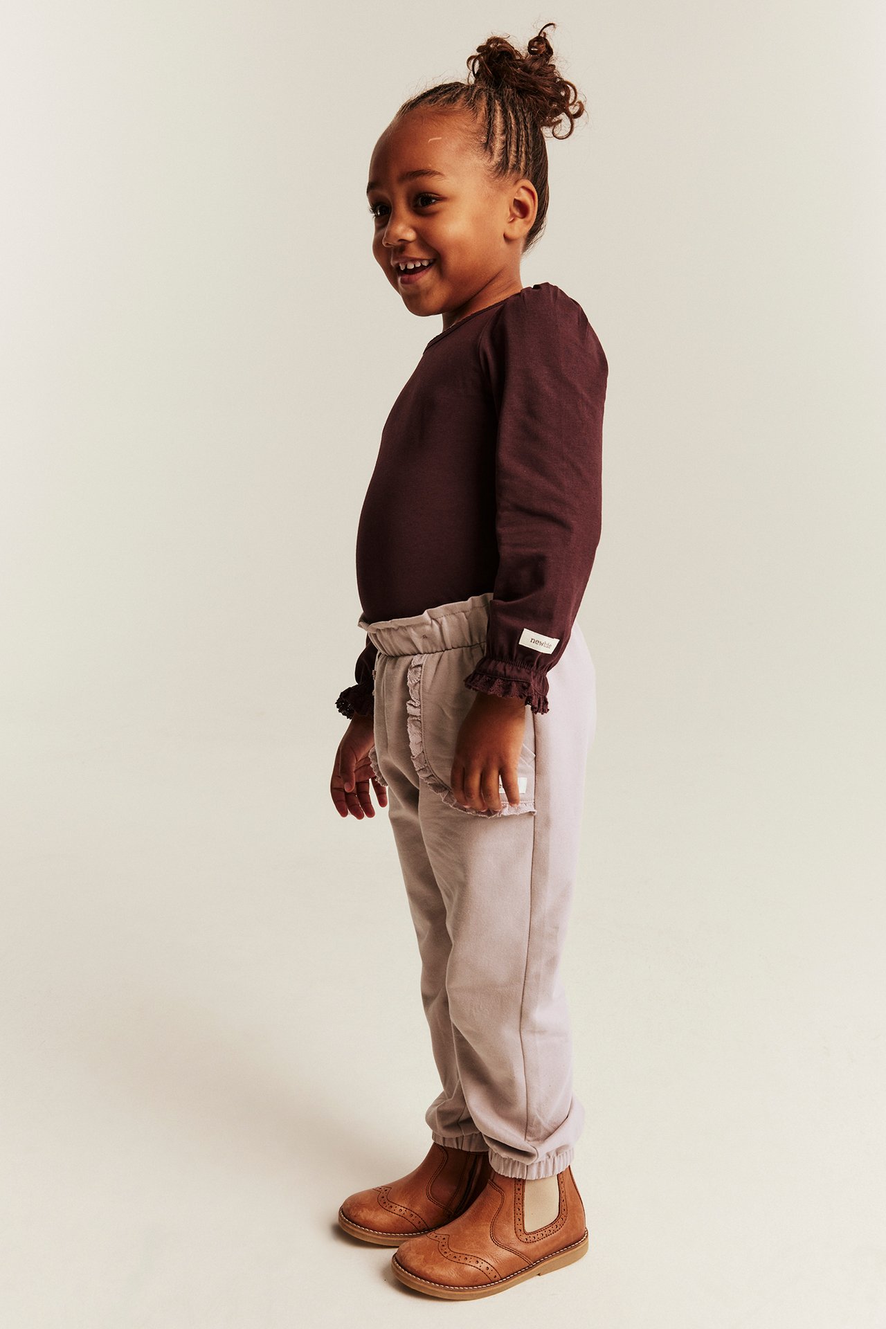 Side view: Kid in burgundy long-sleeve top, light purple sweatpants with ruffles, and brown boots.