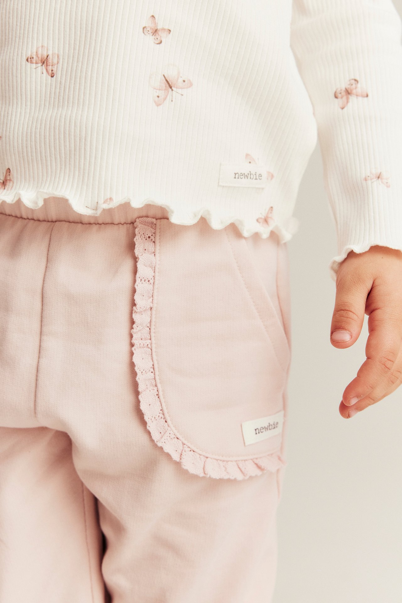 Close-up of baby's light pink jogging bottoms with lace pockets and white ribbed butterfly print top.