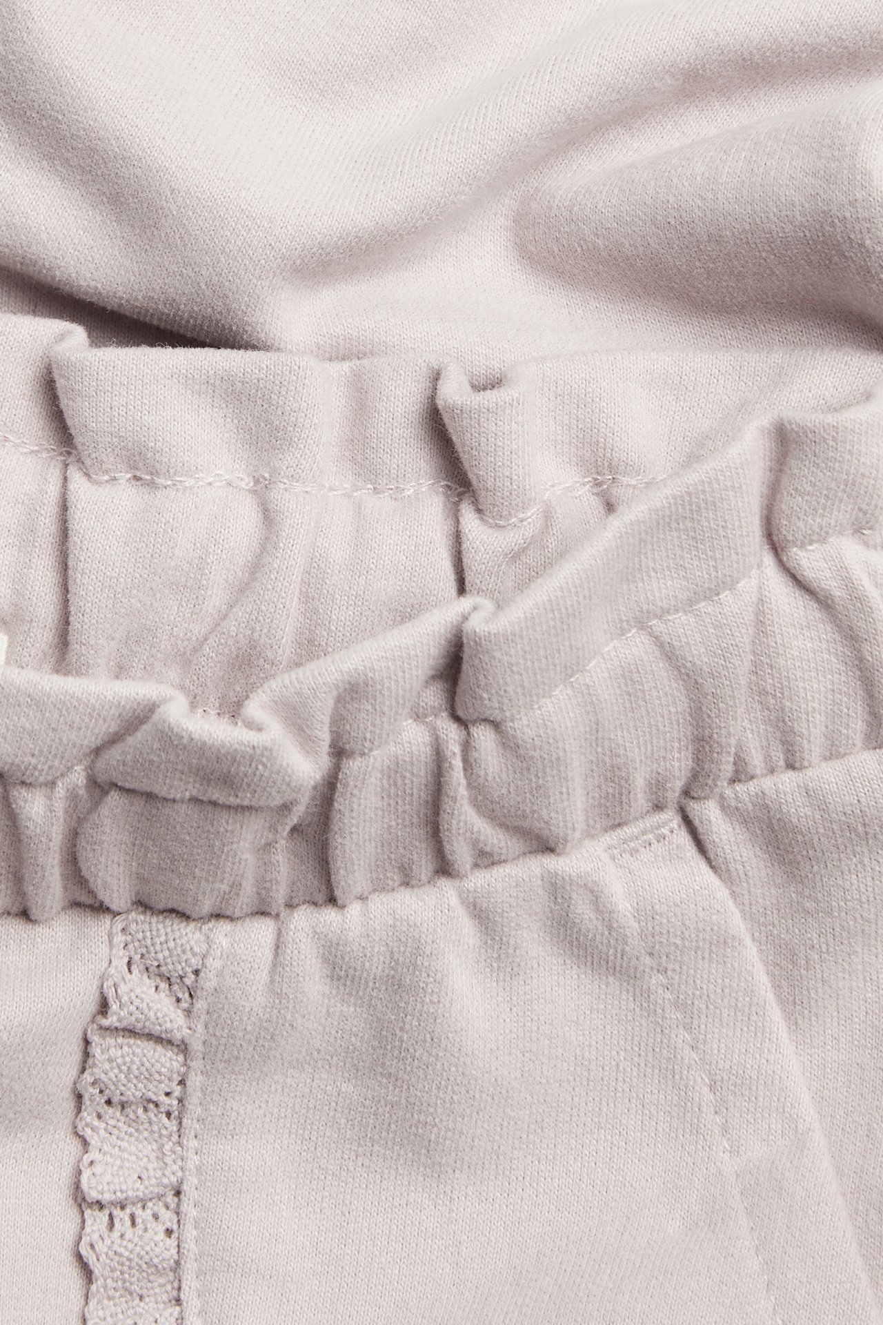 Nahaufnahme von helllila Kinder-Jogginghose aus Baumwolle mit Gummizugbund und spitzenbesetzter Tasche.