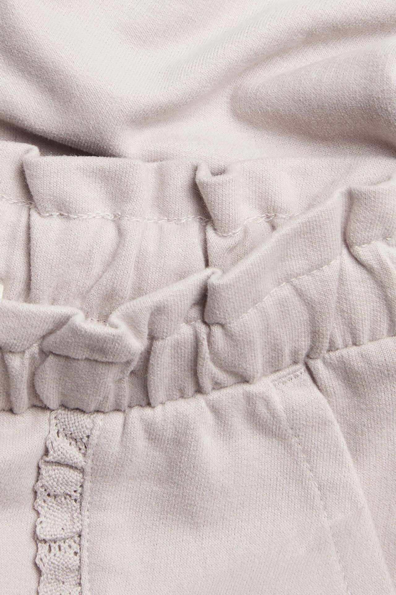 Nahaufnahme von helllila Kinder-Jogginghose aus Baumwolle mit Gummizugbund und spitzenbesetzter Tasche.