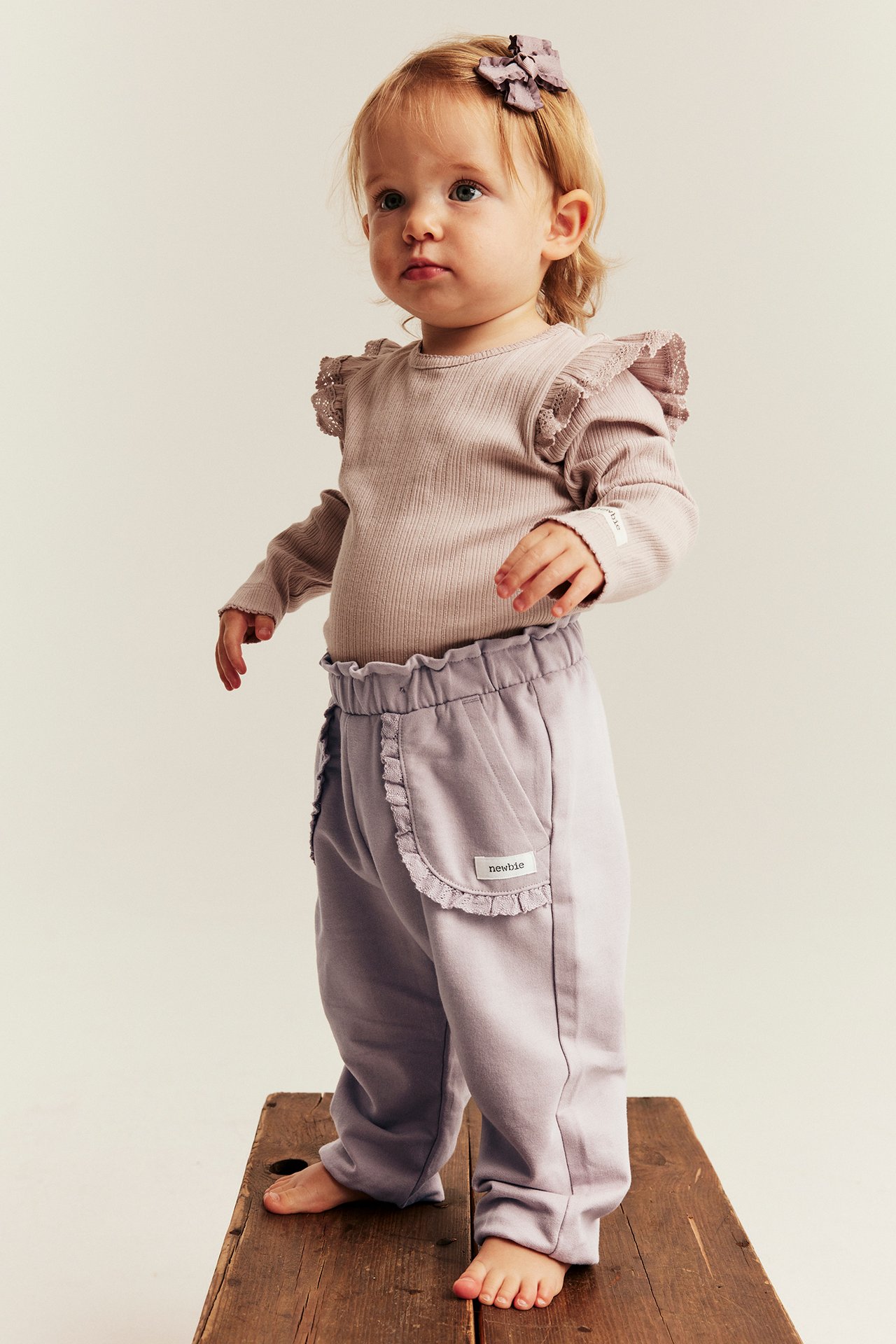 Front view, baby in light purple ruffled sweatpants, ribbed bodysuit, and purple hair bow.