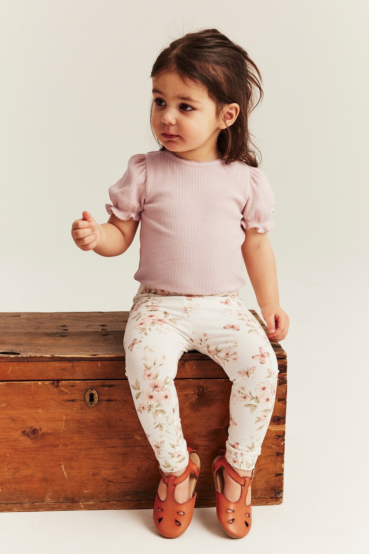 Front view of a kid wearing a light pink ribbed puff-sleeve bodysuit, white floral leggings, and brown T-bar shoes.