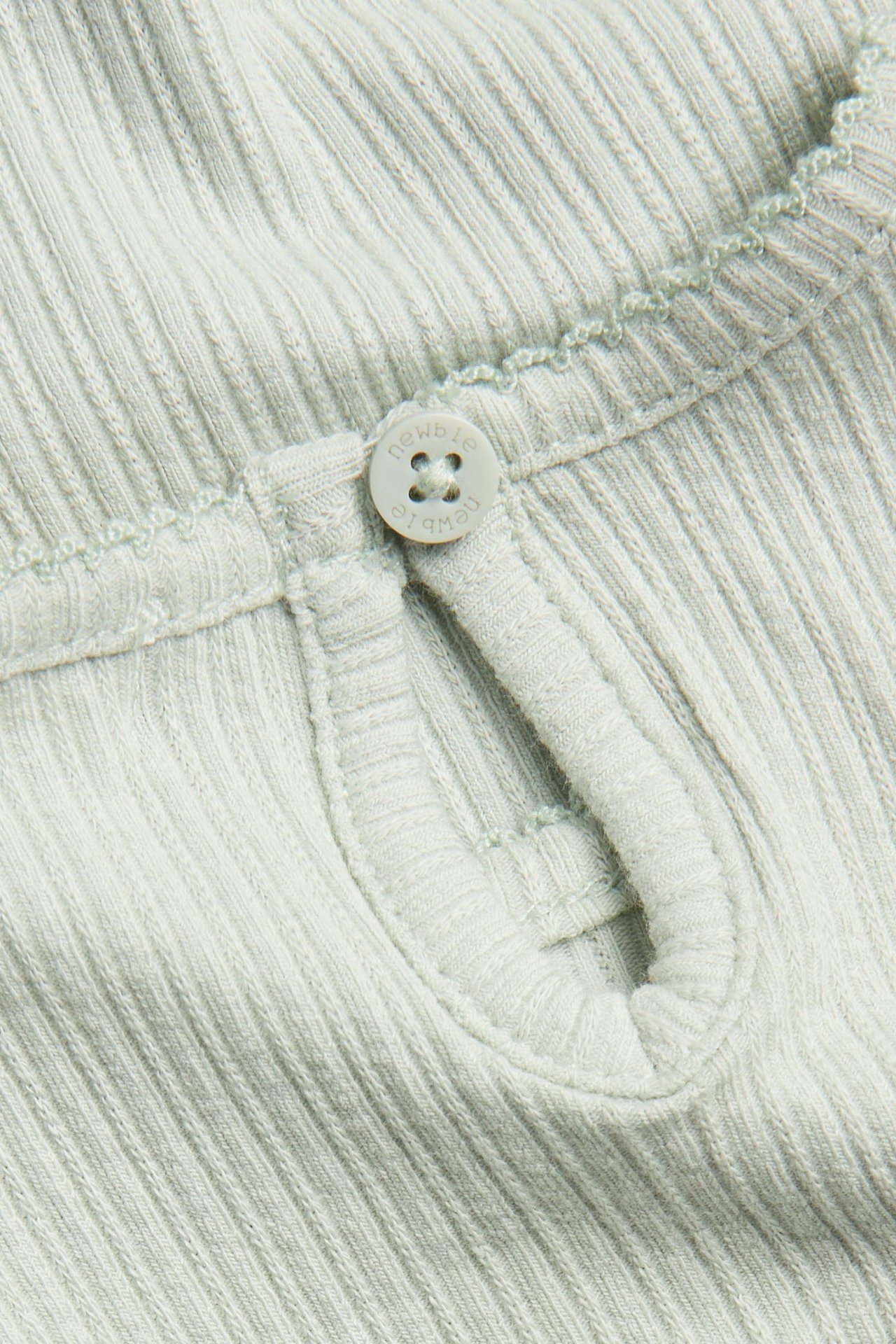 Close-up of a light green ribbed jersey bodysuit's back opening, featuring a button and elastic loop.