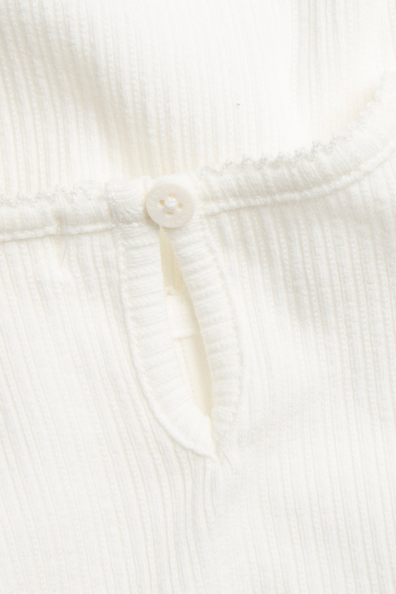Close-up of an off-white ribbed jersey bodysuit, featuring a keyhole opening with a button and picot trim.