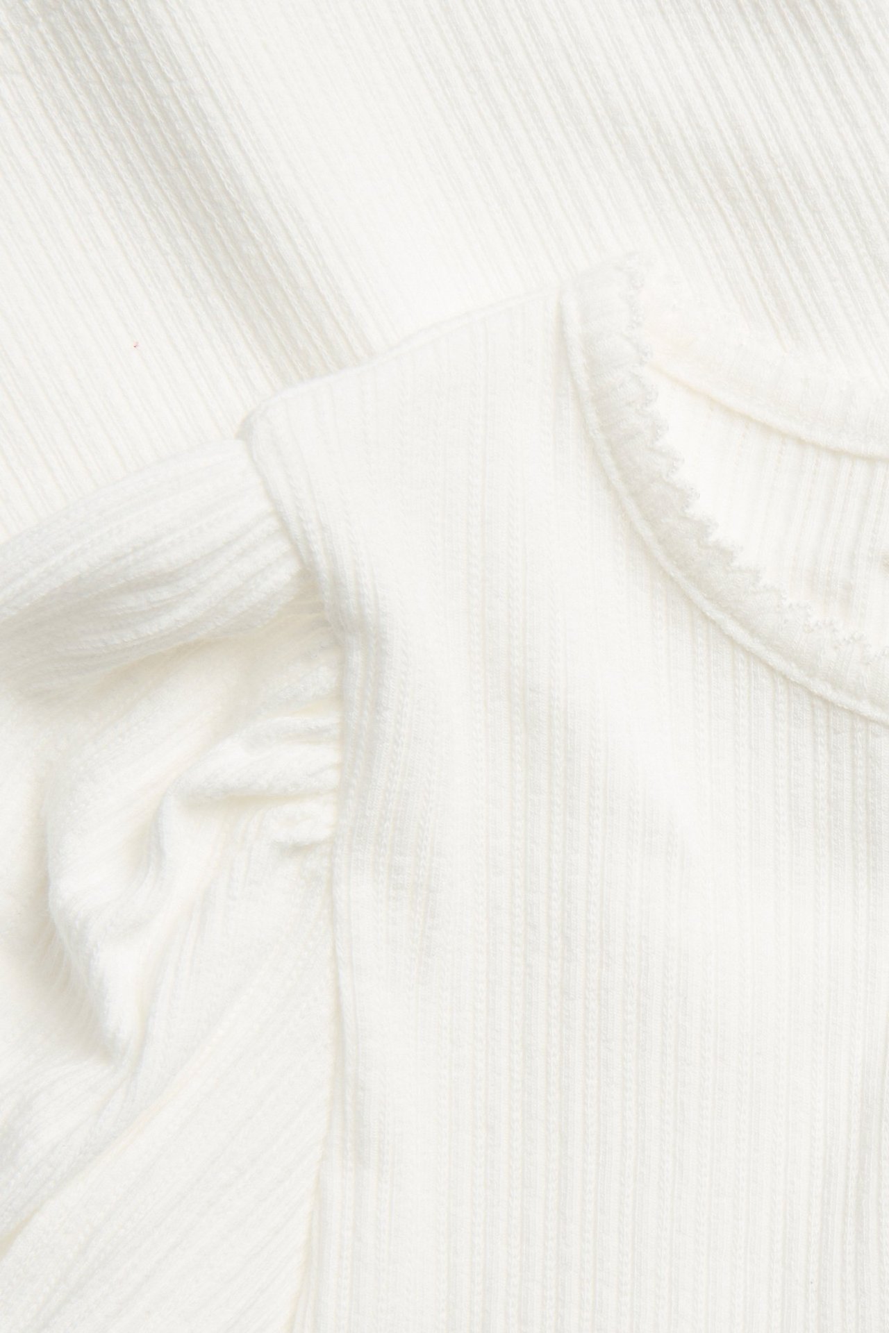 Nahaufnahme eines cremeweißen gerippten Jersey-Kurzarmtops mit Puffärmeln und Picotrand an Hals und Ärmeln.