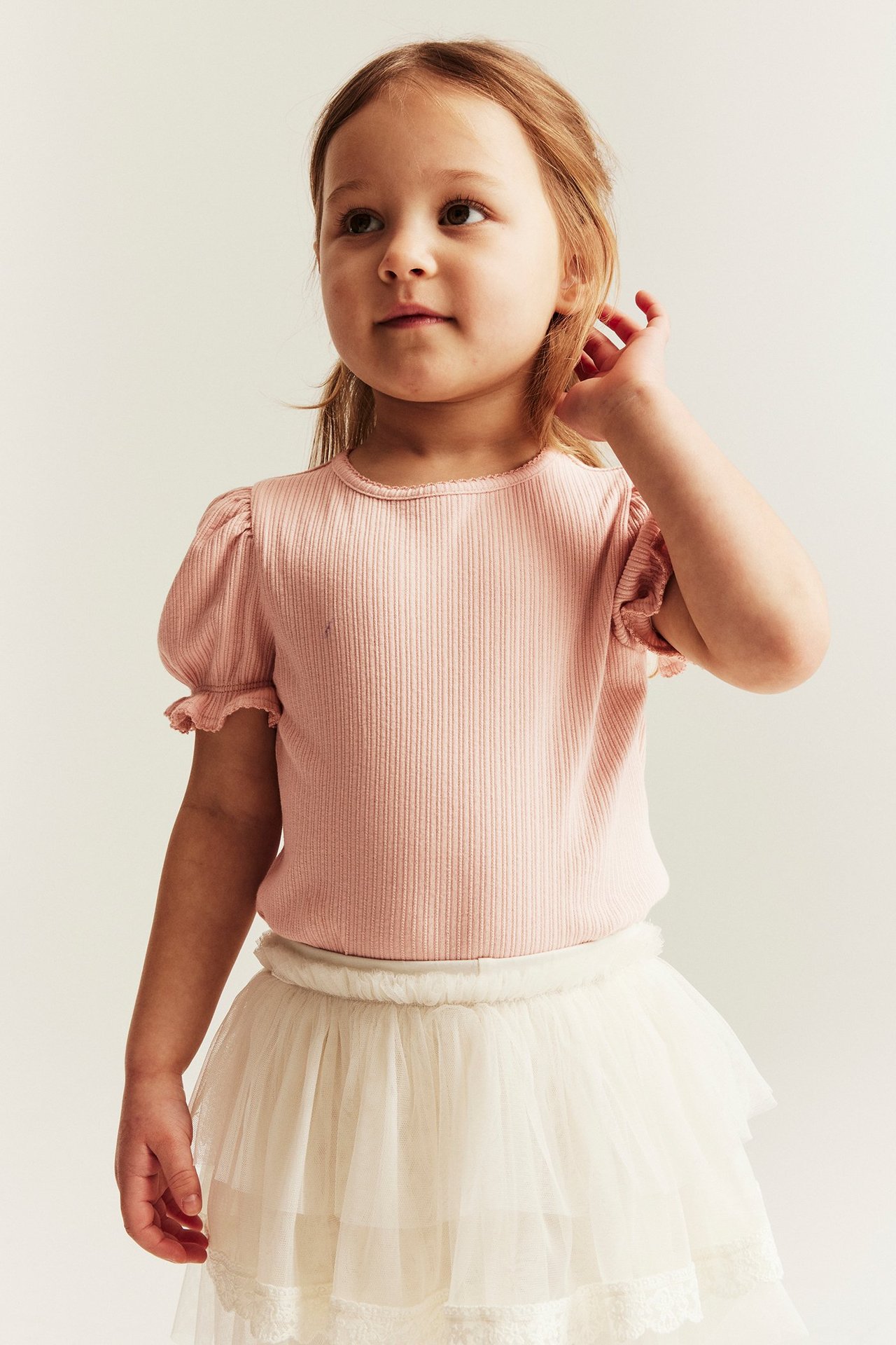 Front view: kid in light pink ribbed puff-sleeve top and white tiered tulle skirt.