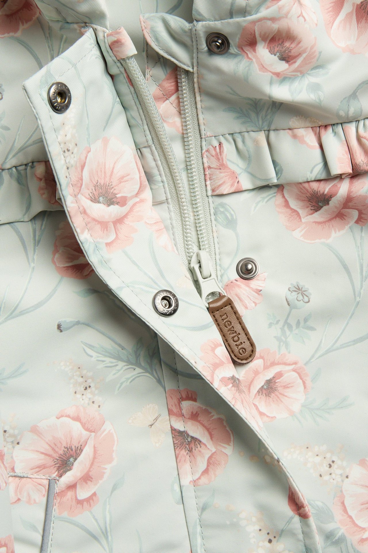 Close-up of a kid's light green floral windproof jacket with pink poppies, a front zipper, and frill details.