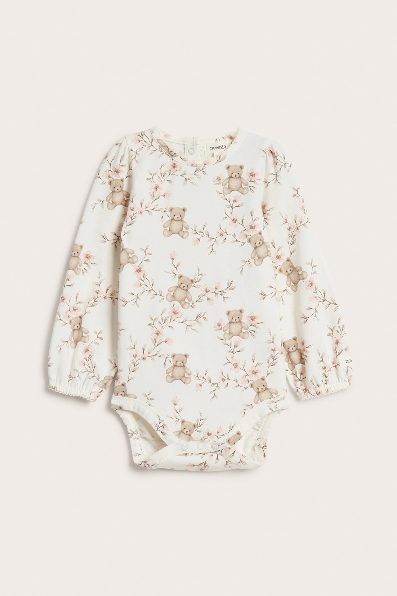 Front view: Off-white baby long-sleeved bodysuit with floral and teddy bear print, snap fasteners.